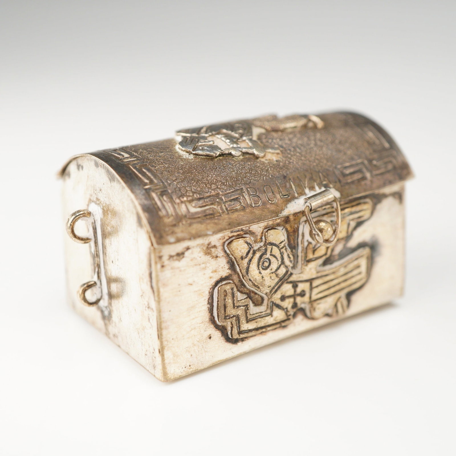 Bolivian 925 Sterling Silver Miniature Trunk Form Trinket Box: This miniature 925 sterling silver trinket box is designed in the form of a treasure chest or trunk. The item features a domed lid and is decorated with traditional Pre-Columbian motifs characteristic