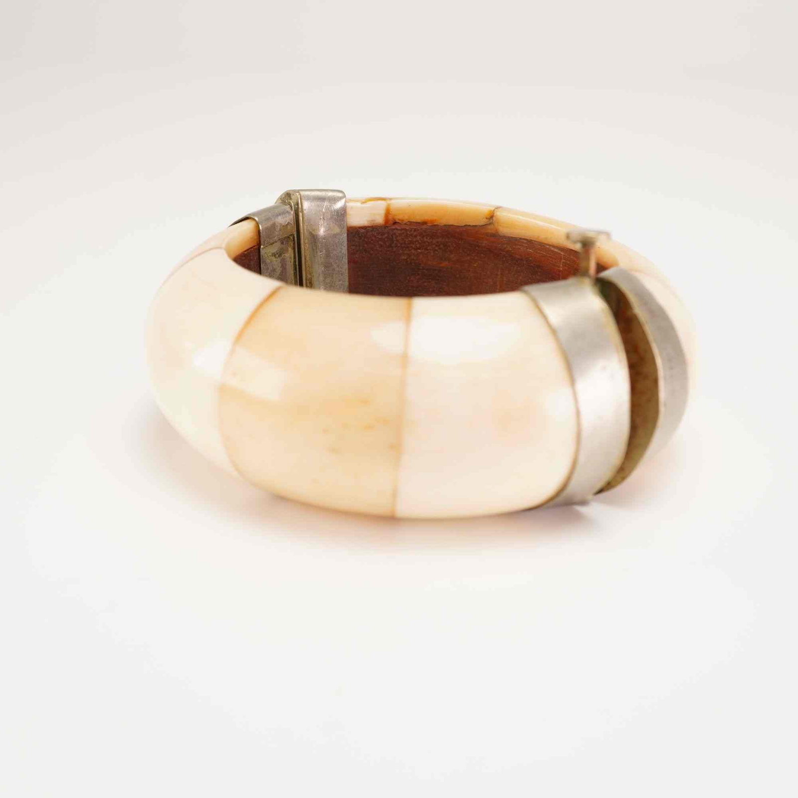 Bone Panel Hinged Bangle Bracelet with Silver-Tone Metal Frame: A vintage hinged bangle bracelet featuring polished, cream-colored bone panels. The organic segments are fitted onto a silver-tone metal frame, creating a chunky, convex profile. The interior is lined