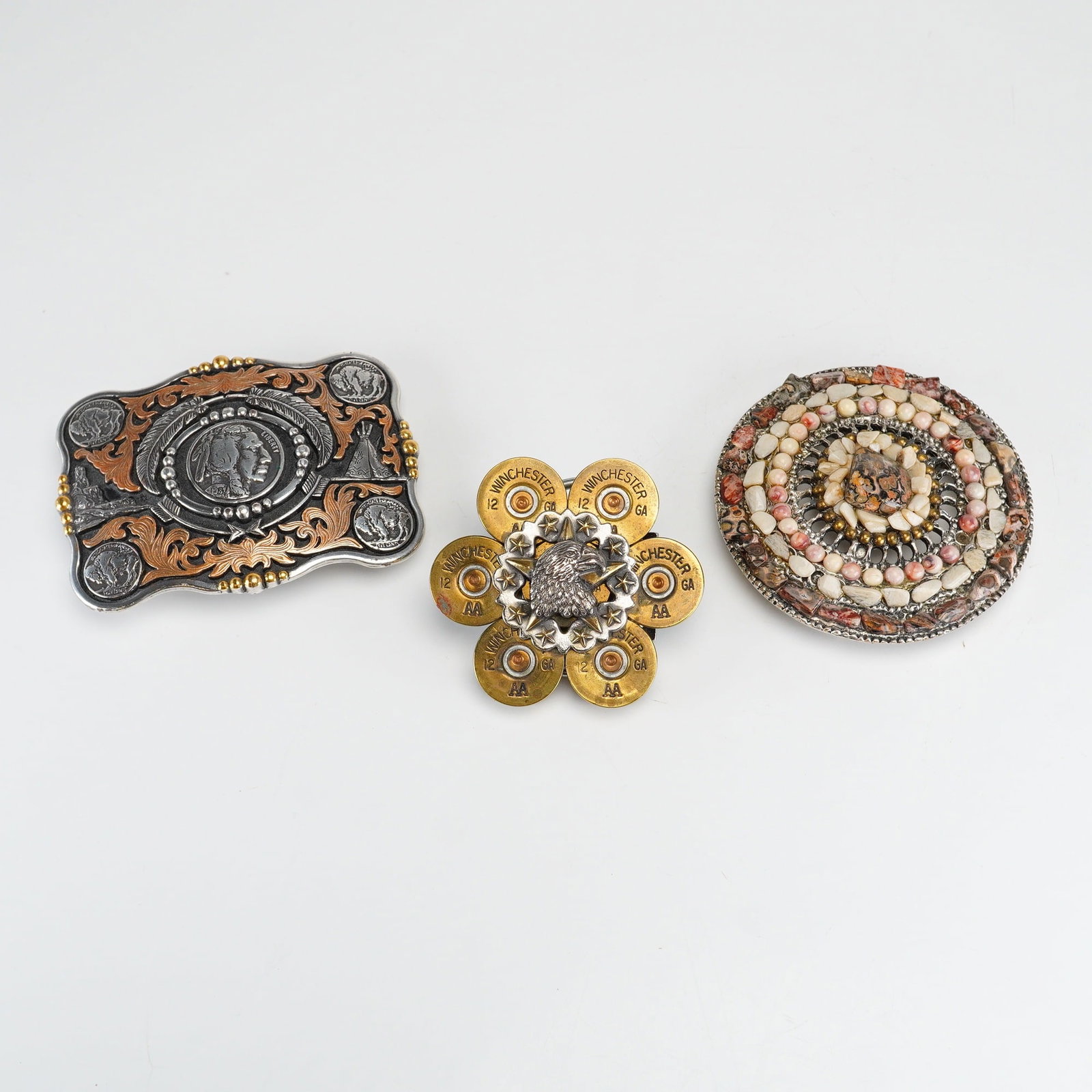 A Trio of Western and Novelty Metal Belt Buckles: A trio of metal belt buckles featuring Western and sporting motifs. The first buckle is a rectangular Western-style piece with scalloped edges and a mixed silvertone and copper-toned finish. The desig