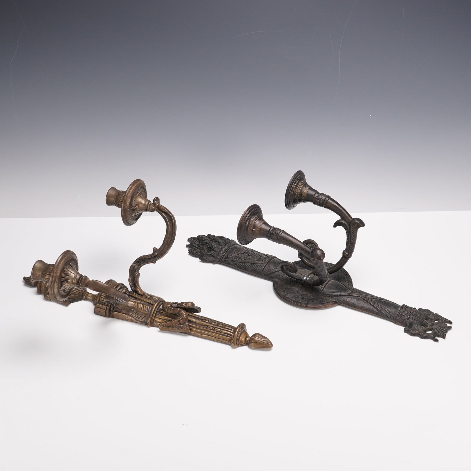2pc Cast Metal Neoclassical Style Wall Sconces: This lot features two cast metal wall sconces, each designed for two candles. One example features classical motifs with urn finial, drapery details, and scrolling candle arms. The other has a more or