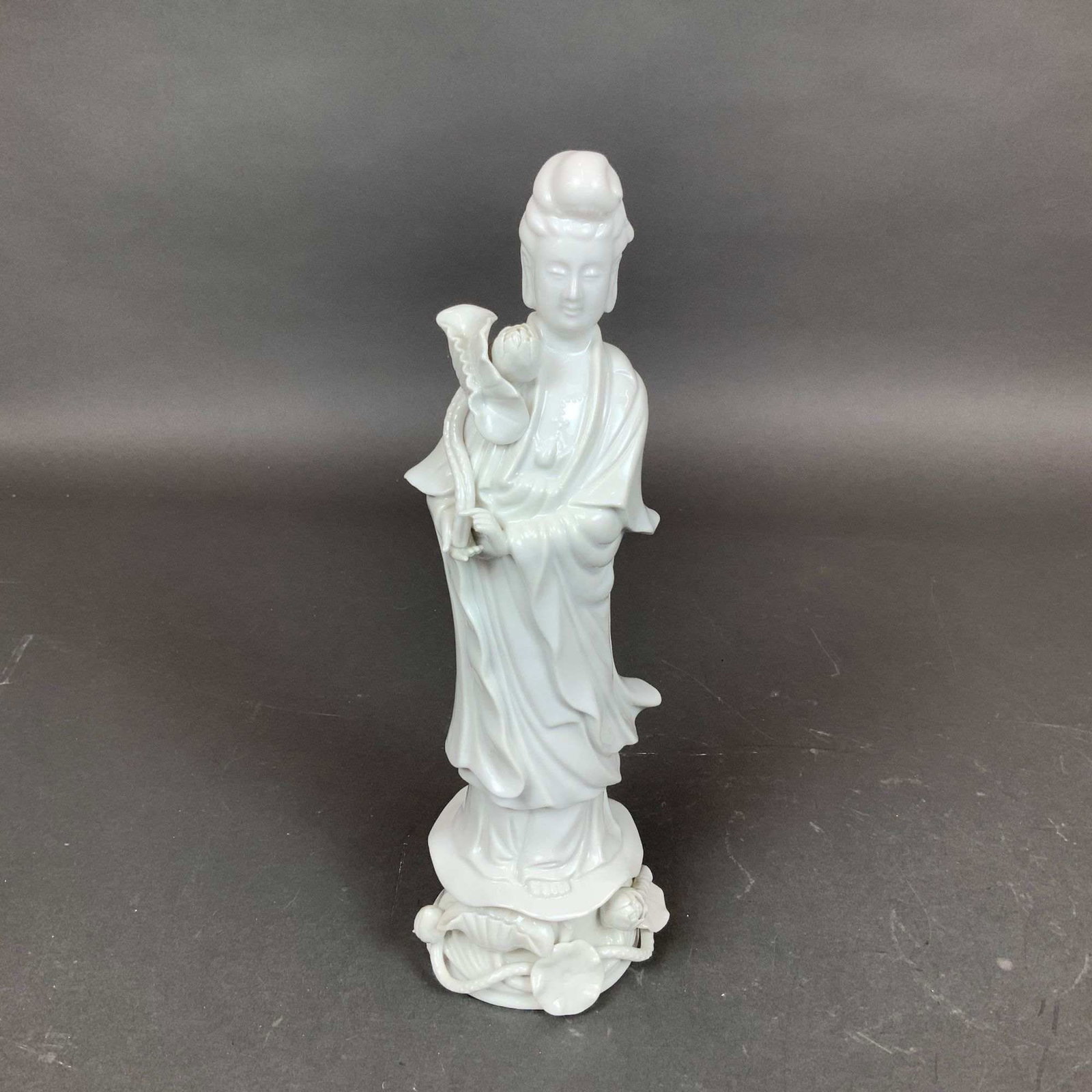 Blanc de Chine Style Porcelain Figure of Goddess Guanyin: This porcelain figure of Goddess Guanyin is modeled in the Dehua or Blanc de Chine style, featuring a monochrome creamy white glaze. The figure is depicted standing and dressed in long, flowing robes 