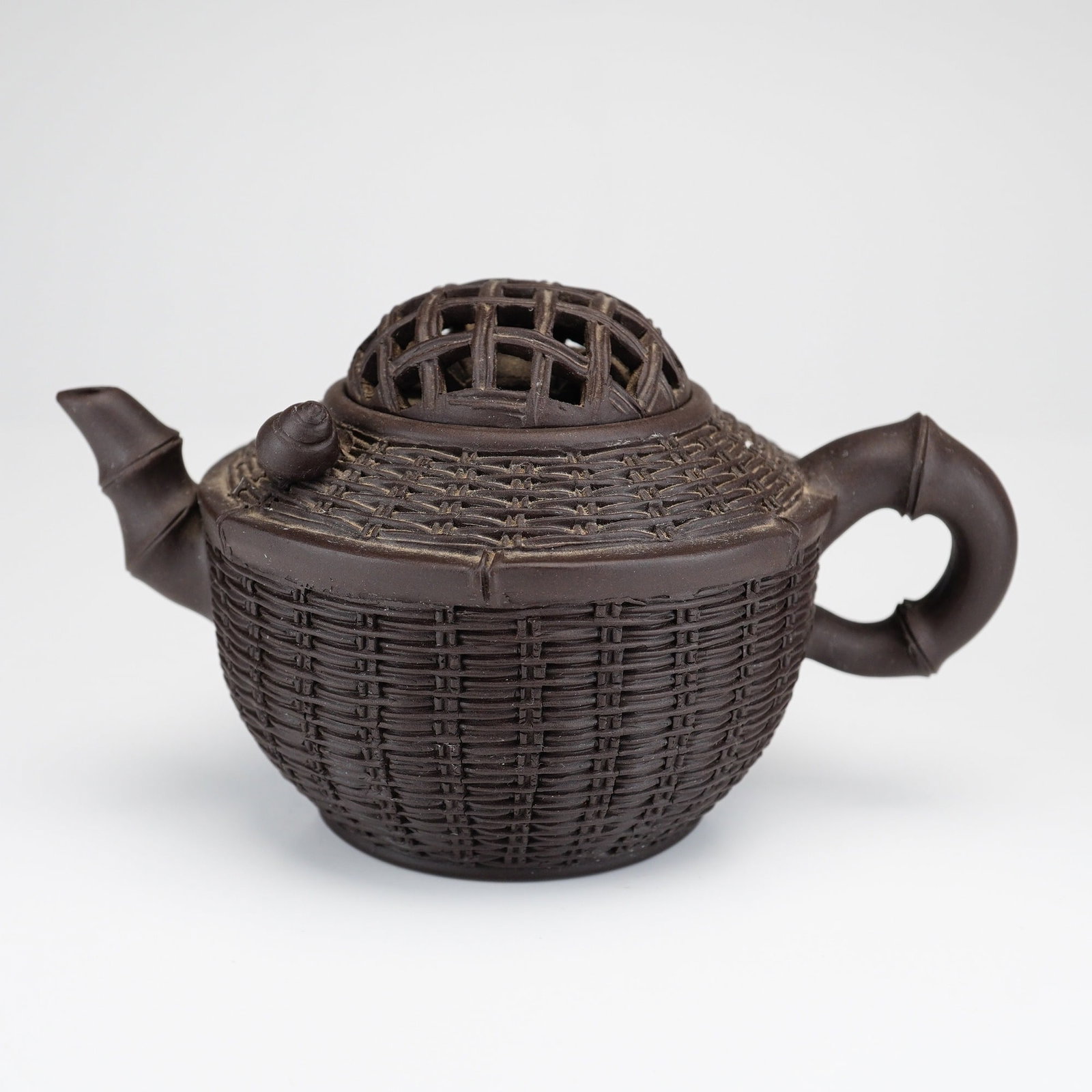 Chinese Yixing Zisha Bamboo Basket Form Teapot: A Chinese Yixing zisha stoneware teapot expertly modeled in the form of a woven bamboo basket. The dark brown, unglazed body features a meticulous all-over relief pattern mimicking basketry. Both the 