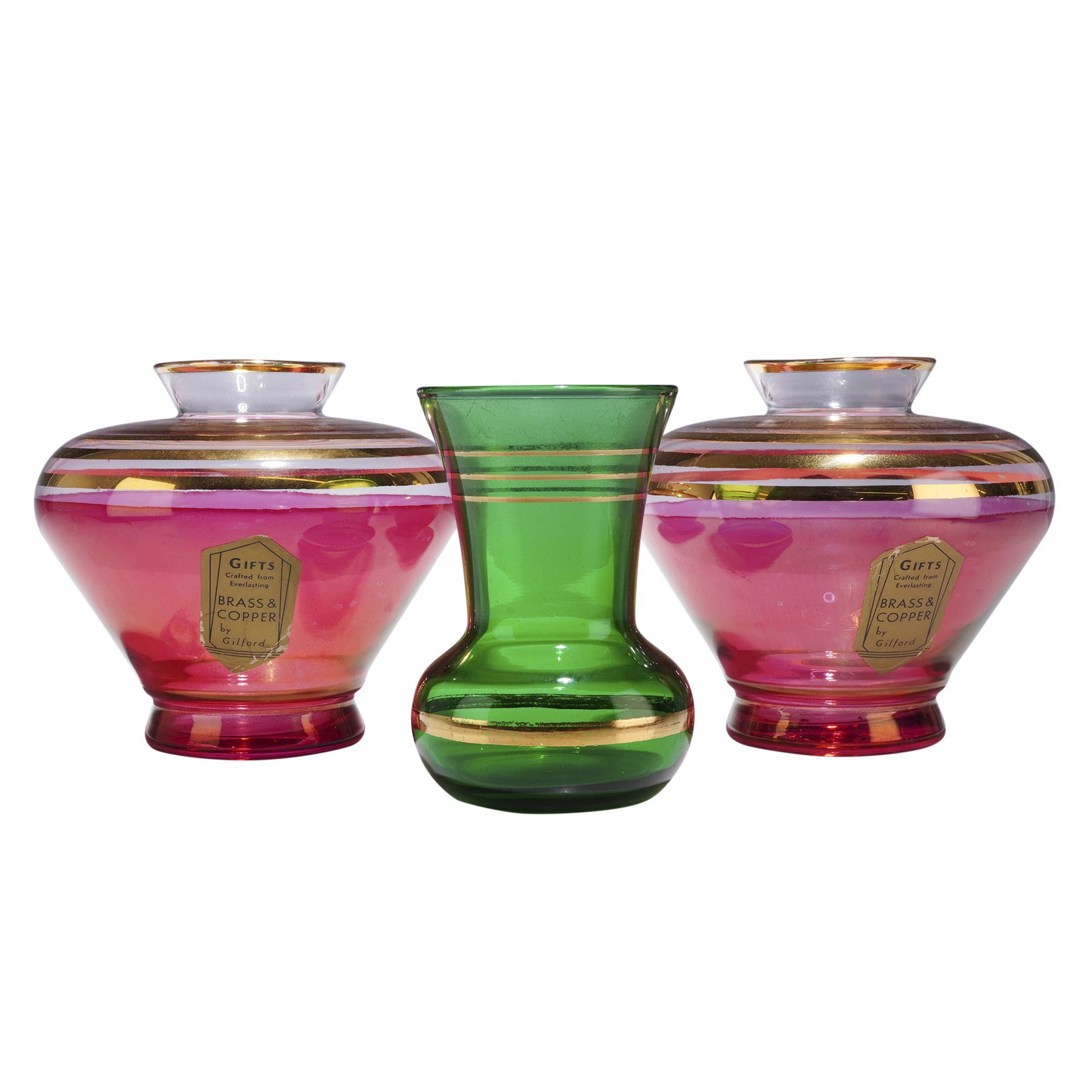 Three Gilt Decorated Glass Vases including Gilford Pink Examples: A collection of three mid-century modern glass vases featuring gilded decoration. The group consists of two larger pink vases and one smaller green bud vase. The two transparent ruby-pink glass vases 