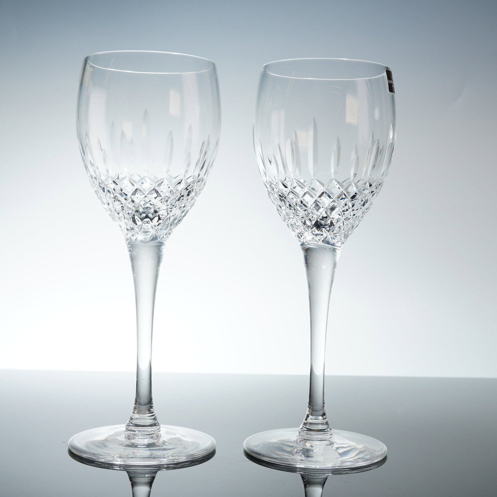 Pair of Dartington Crystal Water Goblets, Coventry: The glasses feature a decorative bowl with a diamond-cut lower register transitioning into vertical wedge cuts. Each vessel is supported by a tall, slender tapered stem and a wide circular foot. The u