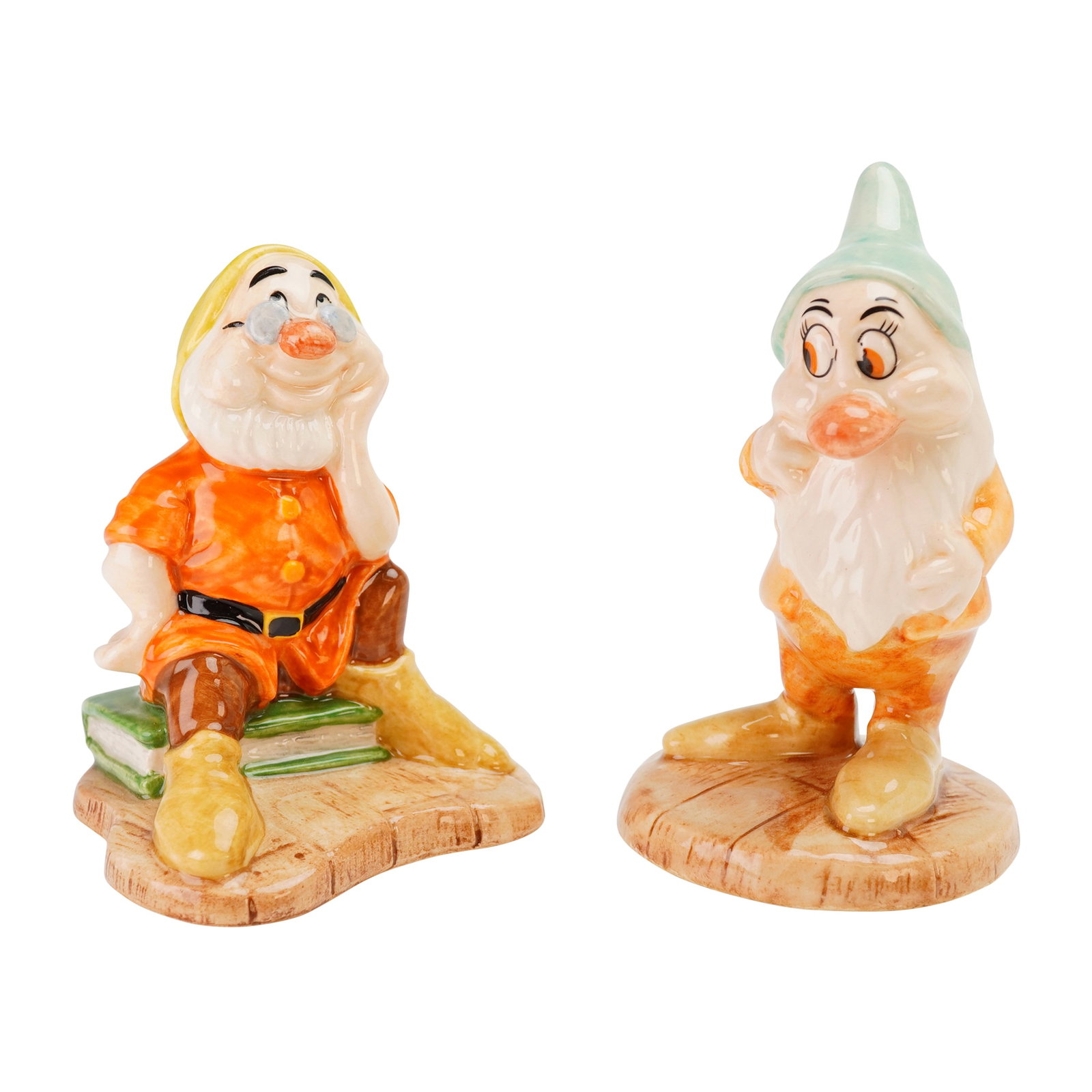 2pc Royal Doulton Disney Snow White Figurines, Bashful SW16 & Doc SW10: These hand-painted glazed ceramic figures are finished with a high-gloss glaze and vibrant colors. The figure of Doc (SW 10) is depicted seated on a stack of books, while Bashful (SW 16) is shown in a