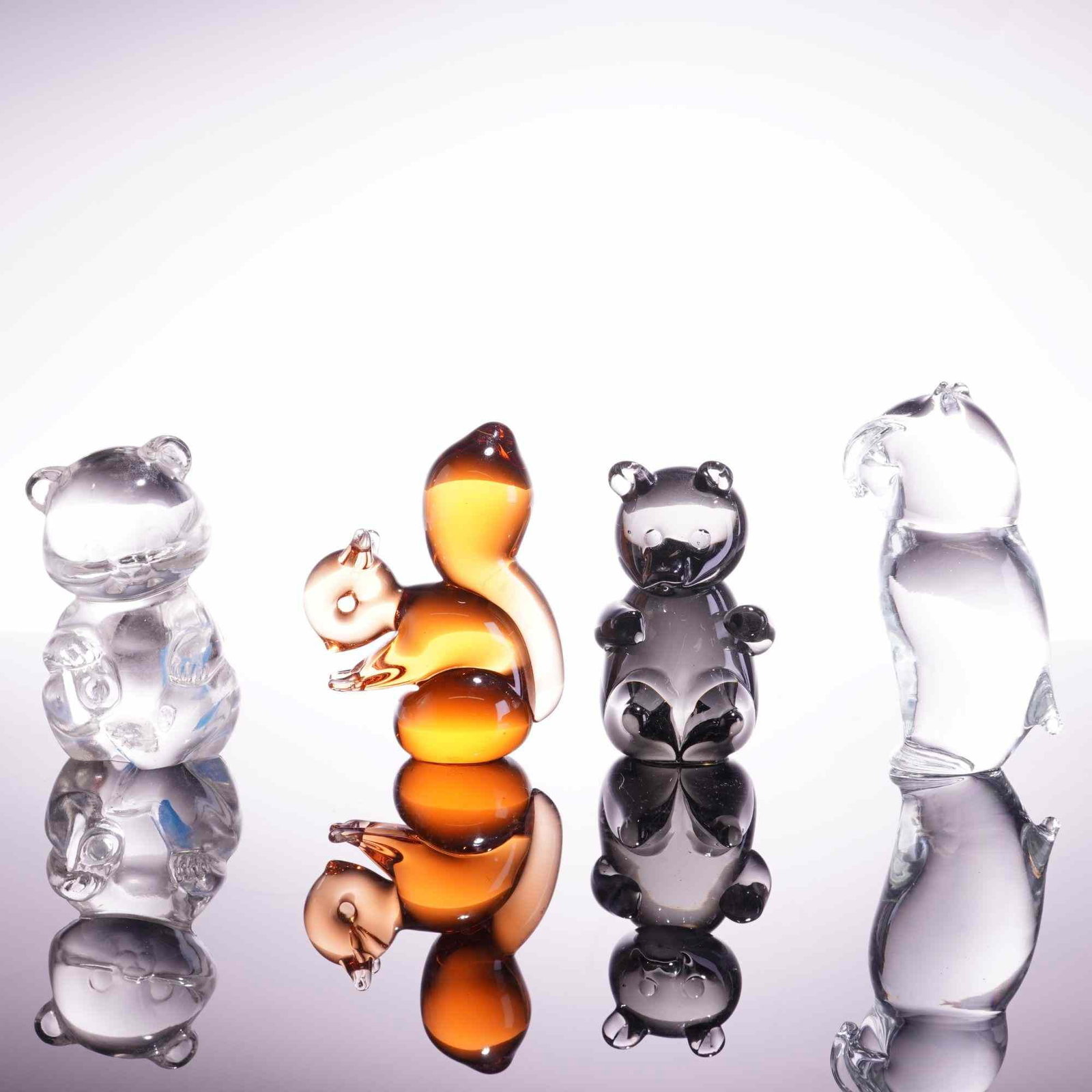 4pc Wedgwood and Fenton Glass Animal Sculptures: A collection of four vintage art glass figurines, featuring stylized animal forms in varied colors and glass types. This group includes an amber glass squirrel figurine etched Wedgwood England on the 