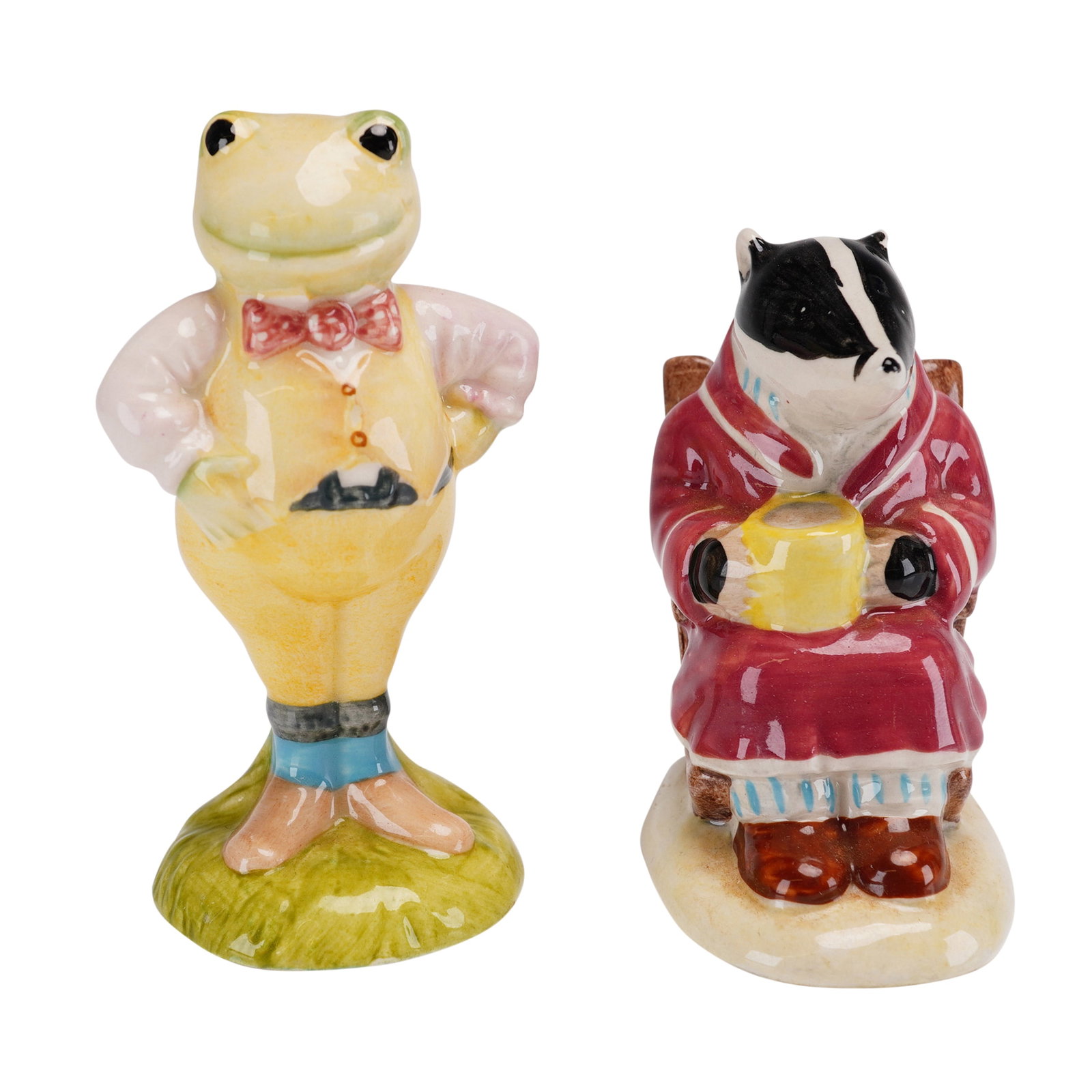 2pc Royal Albert Figurines, Toad (AW1) and Badger (AW2): This pair of fine glazed porcelain figurines was produced by Royal Albert in England as part of The Wind in the Willows series. The set includes Toad (model AW1), depicted in a yellow waistcoat and re