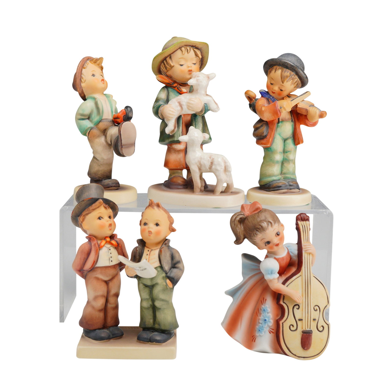 Group of Five Hummel Goebel and Other Ceramic Figurines: A collection of ceramic figurines primarily manufactured by Goebel in the style of M.I. Hummel. The group includes several depictions of children in traditional dress, including a boy marching with an