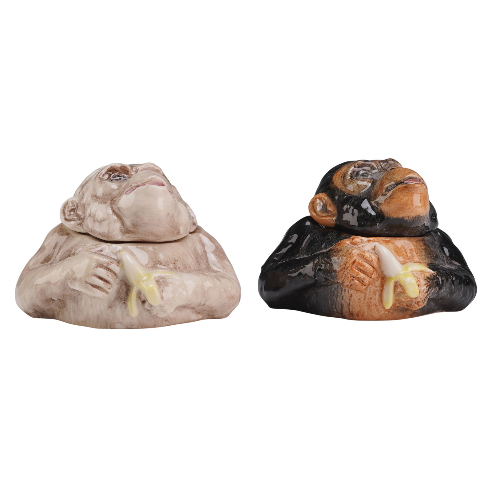 Two Kevin Francis Face Pots, Charles and Camilla Chimpanzees: Each pot is modeled as the upper torso of a chimpanzee holding a partially peeled yellow banana, with the head functioning as a removable lid. Charles is decorated in a black and orange-brown glaze, w
