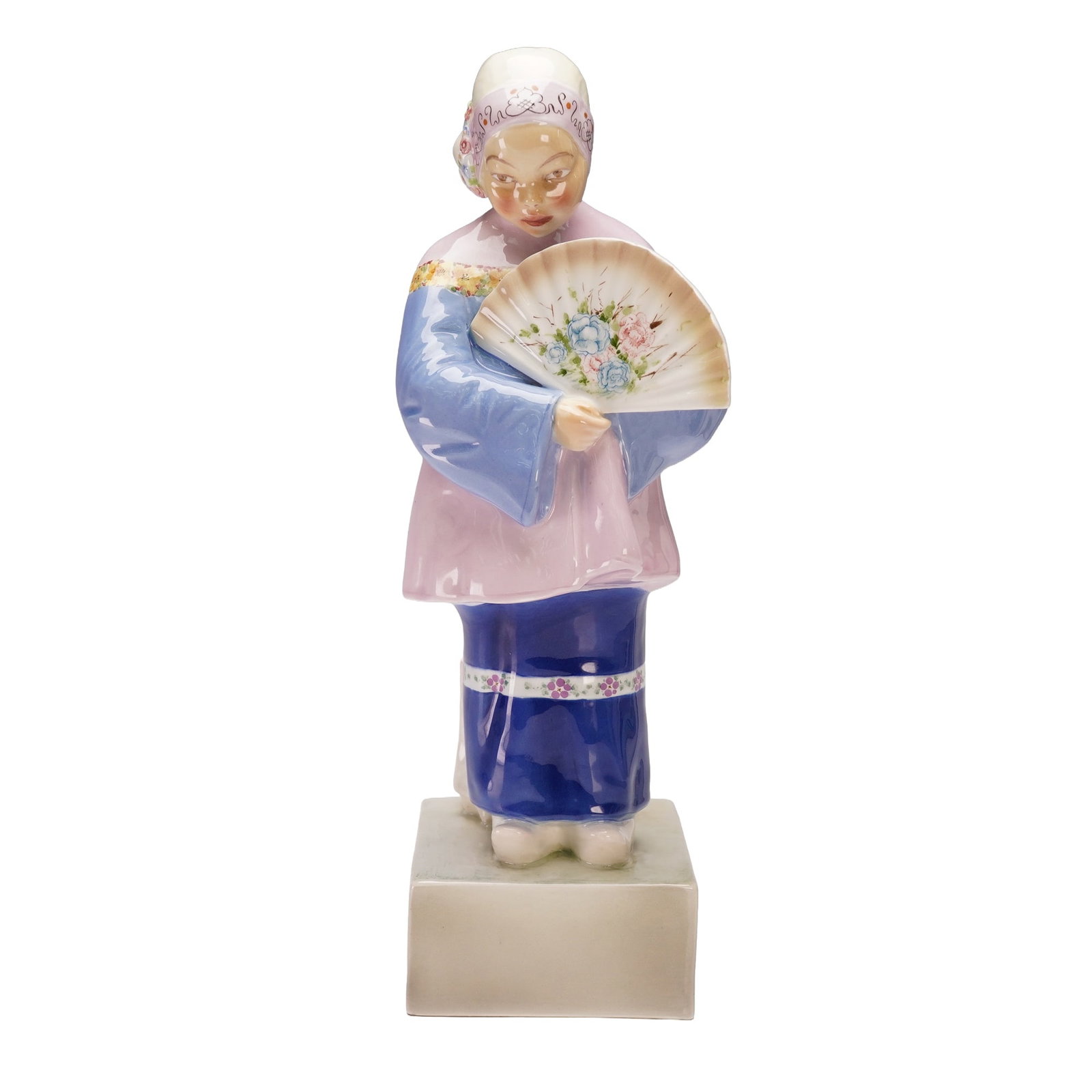 Goldscheider Figurine by Julius Hentschel, Chinese Girl with Fan: A finely modeled Goldscheider porcelain figurine depicting a Chinese girl holding an open fan decorated with floral detail. She wears traditional attire in soft pastel tones of pink, blue, and lavende