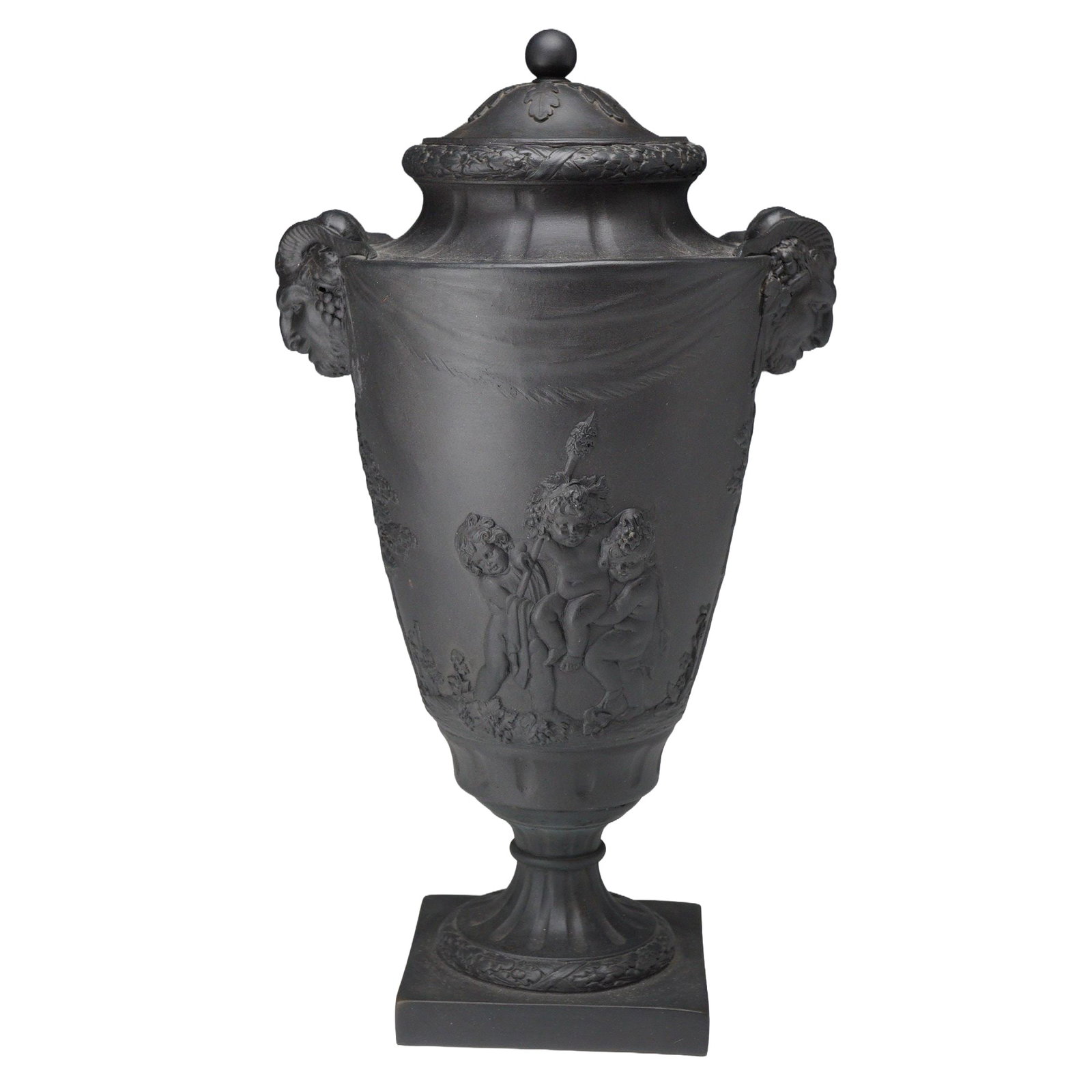 Wedgwood Black Basalt Satyr Head Lidded Urn: This neoclassical lidded urn is crafted from Wedgwood black basalt stoneware, featuring a matte, unglazed black surface. The campana-shaped vessel is set upon a fluted pedestal and a square plinth bas