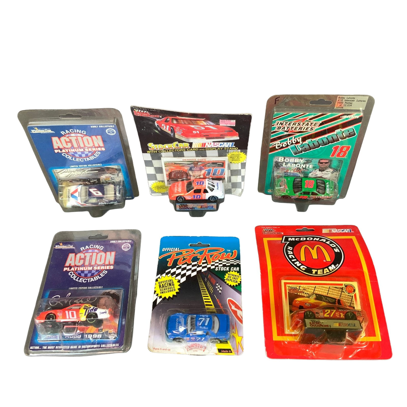 6pc Lot of 1:64 Scale NASCAR Collectible Die-Cast Model Cars: A collection of six vintage NASCAR die-cast model cars in 1:64 scale, each housed in its original blister pack. The assortment includes vehicles from various manufacturers and series prominent in the 