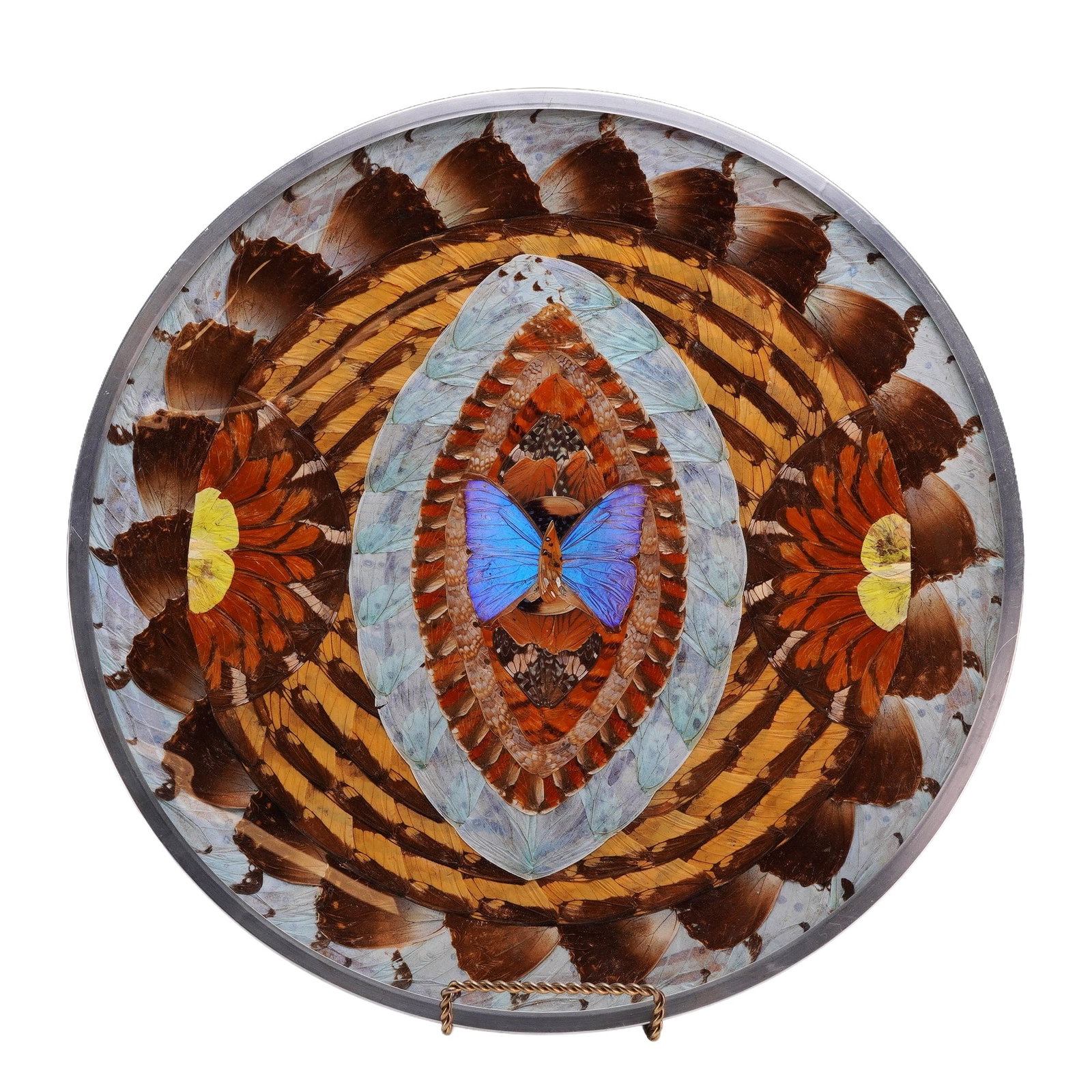 Brazilian Blue Morpho Art Plate with Stand: A circular Brazilian art plate featuring an intricate geometric collage created from real butterfly wings encased under glass. The radial design is composed of concentric bands and almond-shaped patte