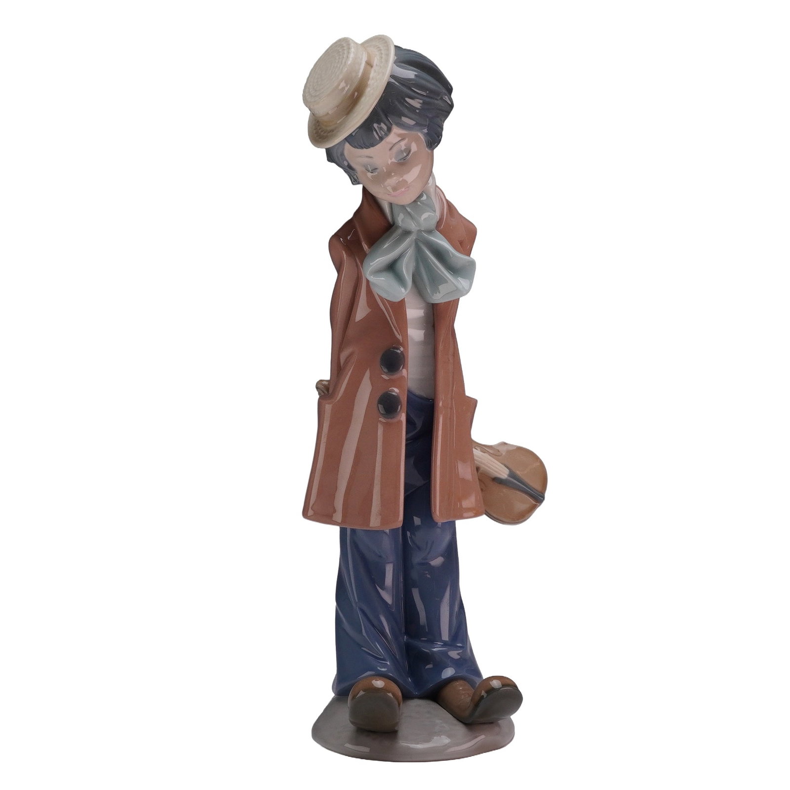 Lladro Porcelain Figurine Clown with Violin 01005057: The piece, designed by Salvador Debon, depicts a young boy dressed as a street performer, wearing a long brown double-breasted overcoat over loose blue trousers and a white shirt with a large pale blu