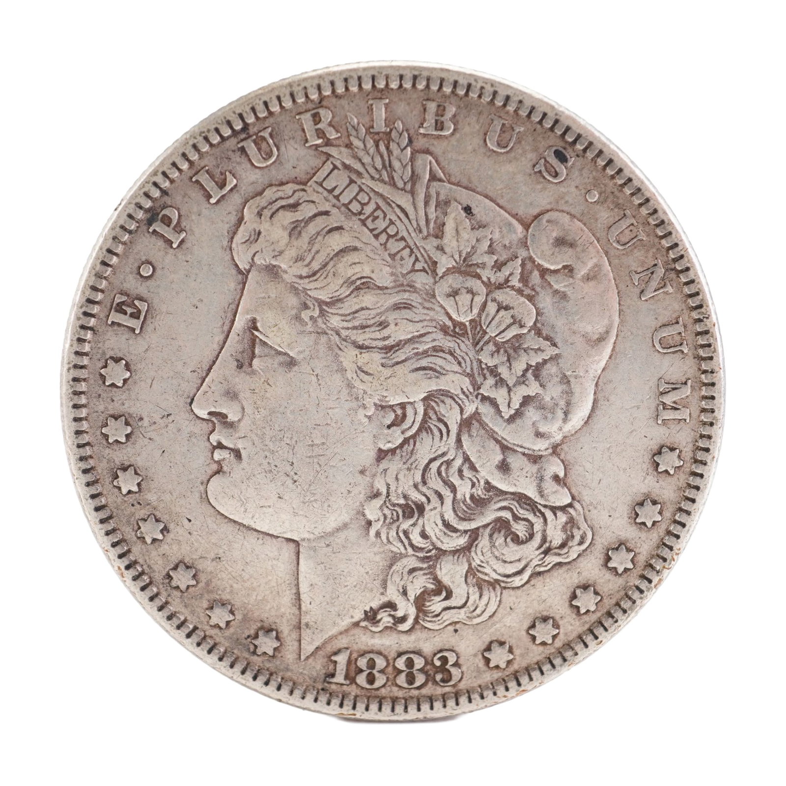 1883 U.S. Morgan Dollar 90% Silver Coin, Circulated: Morgan Dollar with obverse Liberty head, facing left and E PLURIBUS UNUM LIBERTY and date. Revers depicts Eagle holding arrows and an olive branch within wreath. Total weight 26g. Dimensions: 38.1mm D