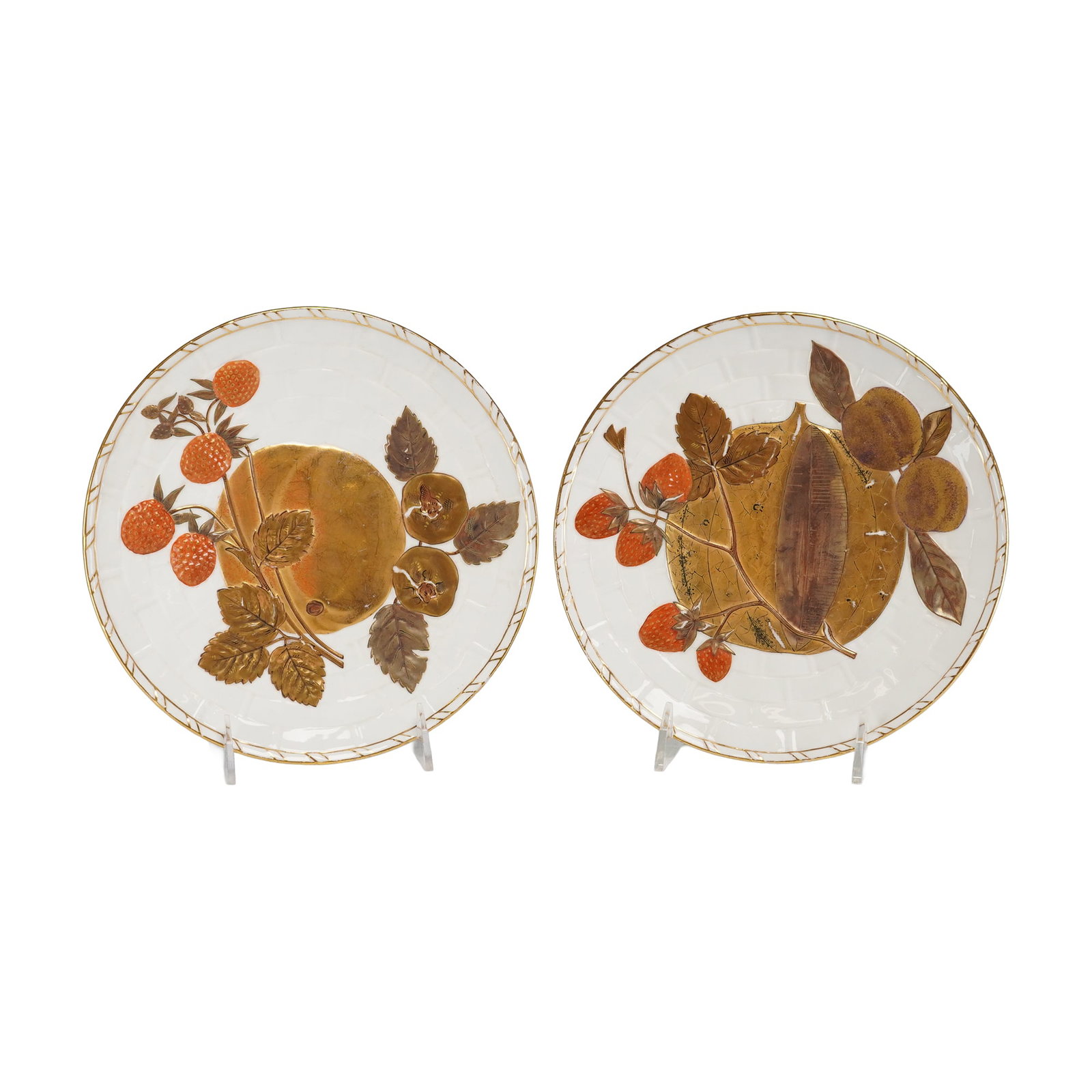 2pc Wedgwood Gilded Fruit Plates: A pair of Wedgwood Gilded Fruit Plates. These circular plates feature a relief pattern with a striped pattern on the rim. One plate depicts a central watermelon with small peaches and strawberries; th