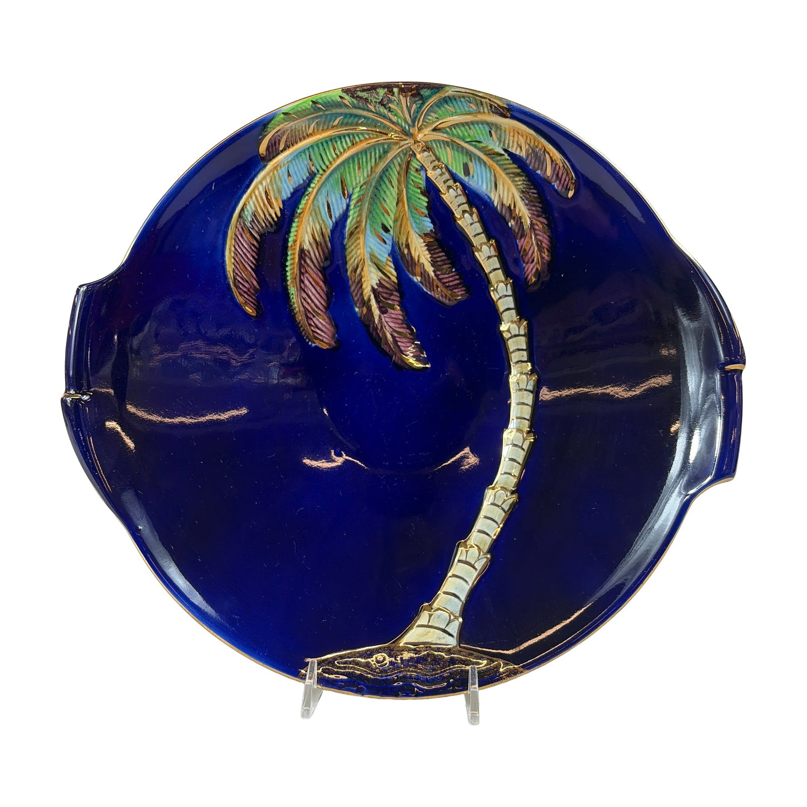Beswick Ware Tropical Palm Tree Dish: The circular vessel features two integral tab handles and a deep cobalt blue glazed interior. The center is decorated with a molded relief scene of a curving palm tree, hand-painted in shades of green