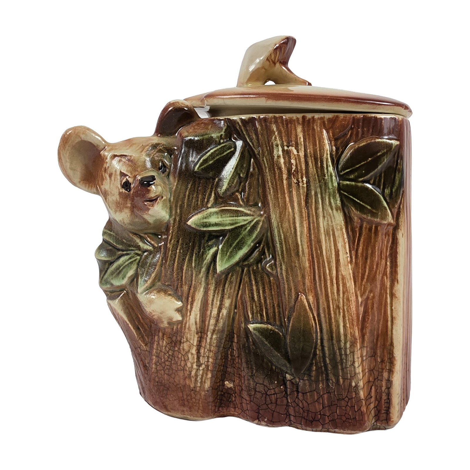 McCoy Ceramic Koala Cookie Jar: The piece is designed in the form of a rustic tree stump or log, featuring relief-molded leaves and a koala bear figure peeking from behind the trunk. The fitted circular lid is topped with a mushroom