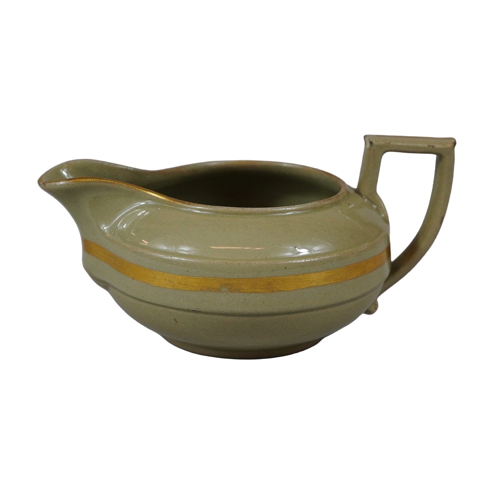 Wedgwood Earthenware Gilded Sage Green Creamer: The piece is constructed from earthenware with a low, squat body featuring a wide spout and a sharp, angular squared handle characteristic of the period. It is finished in a semi-matte sage green glaz