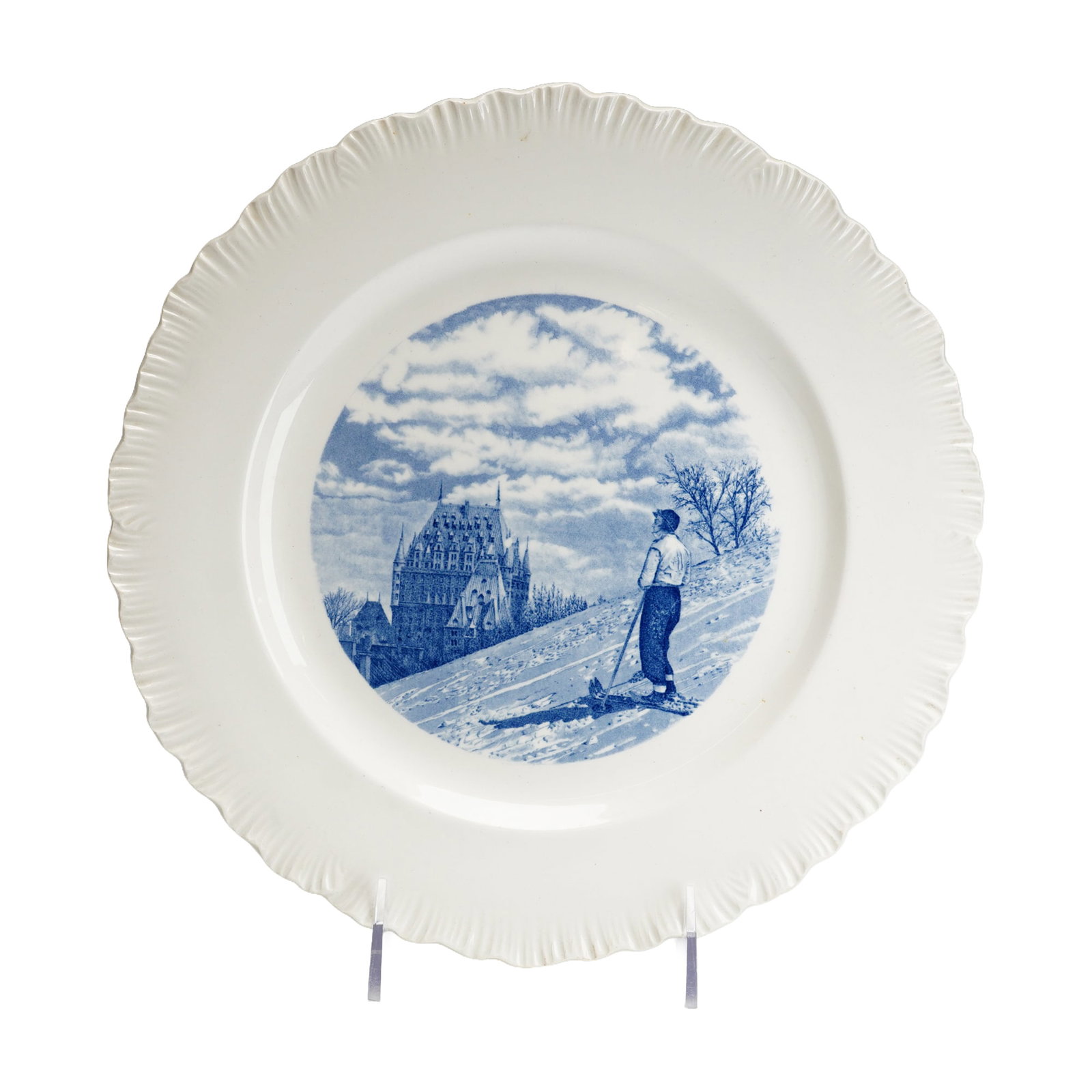 Wedgwood Etruria Blue and White Transfer-Printed Chateau Frontenac Quebec Plate: This plate is a souvenir item manufactured by Wedgwood in England, part of a series depicting Canadian skiing scenes. The object is constructed from cream-colored earthenware and features a molded, fl