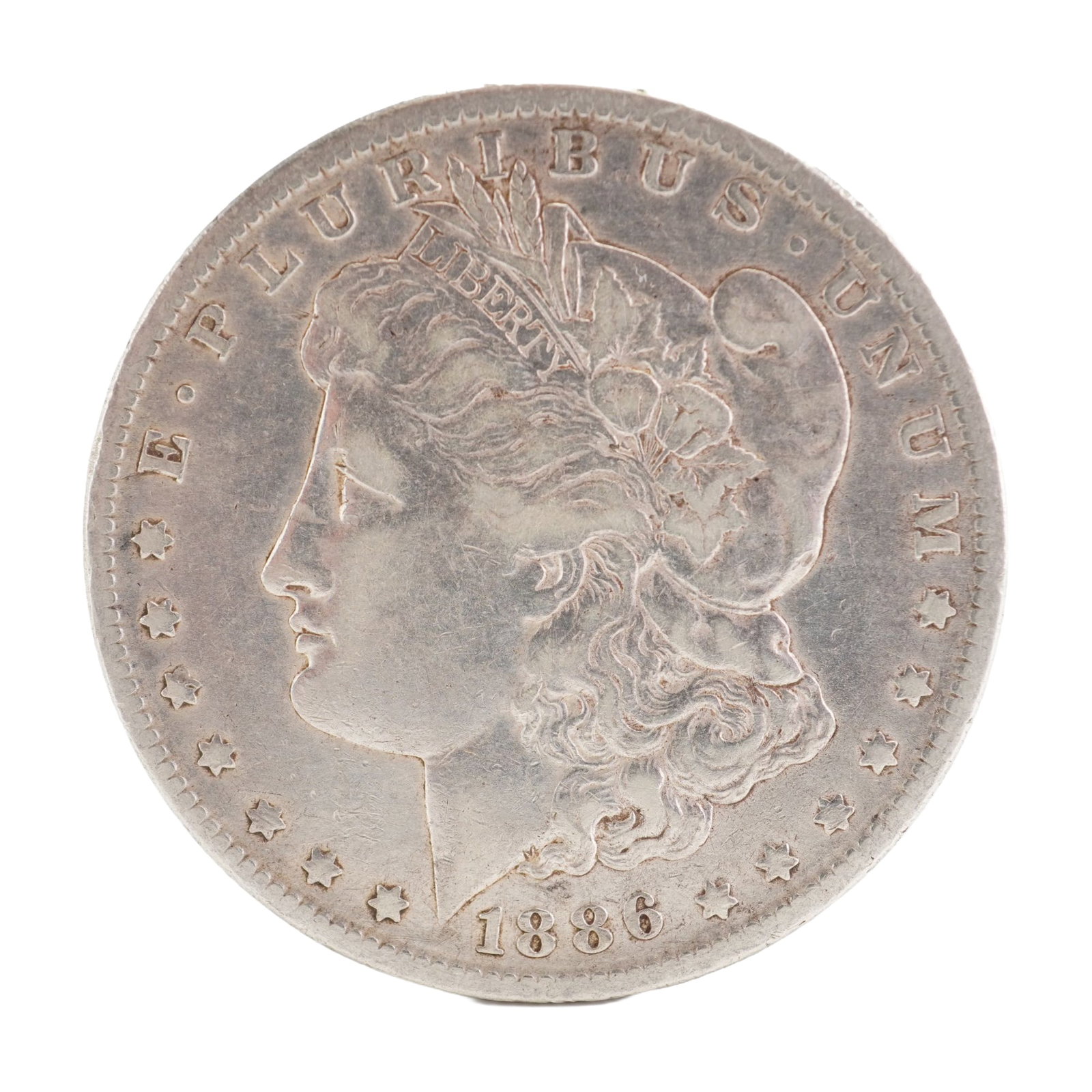 1886 U.S. Morgan Dollar 90% Silver Coin, Circulated: Morgan Dollar with obverse Liberty head, facing left and E PLURIBUS UNUM LIBERTY and date. Revers depicts Eagle holding arrows and an olive branch within wreath. Total weight 26g. Dimensions: 38.1mm D
