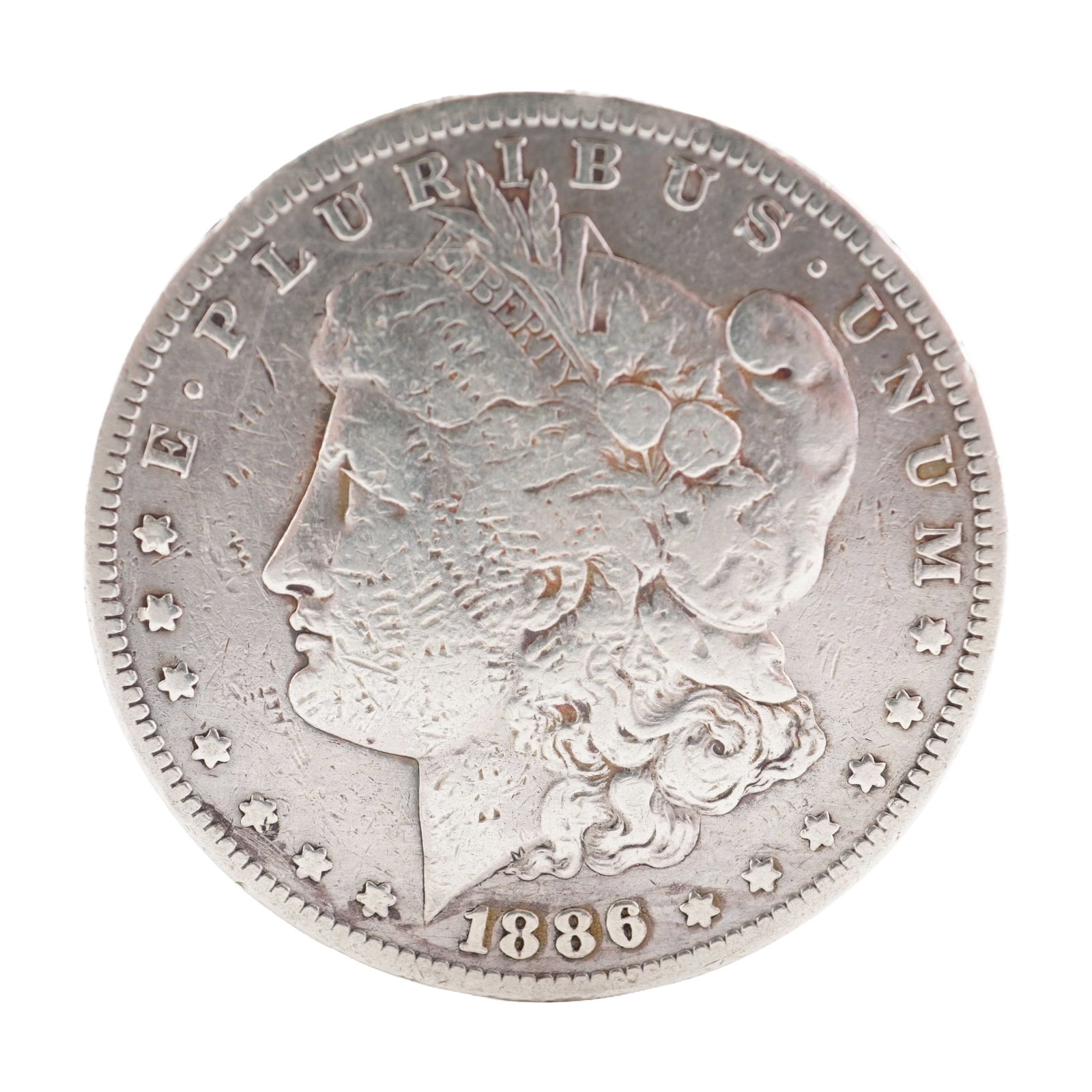1886 U.S. Morgan Dollar 90% Silver Coin, Circulated: Morgan Dollar with obverse Liberty head, facing left and E PLURIBUS UNUM LIBERTY and date. Revers depicts Eagle holding arrows and an olive branch within wreath. Total weight 22g. Dimensions: 38.1mm D