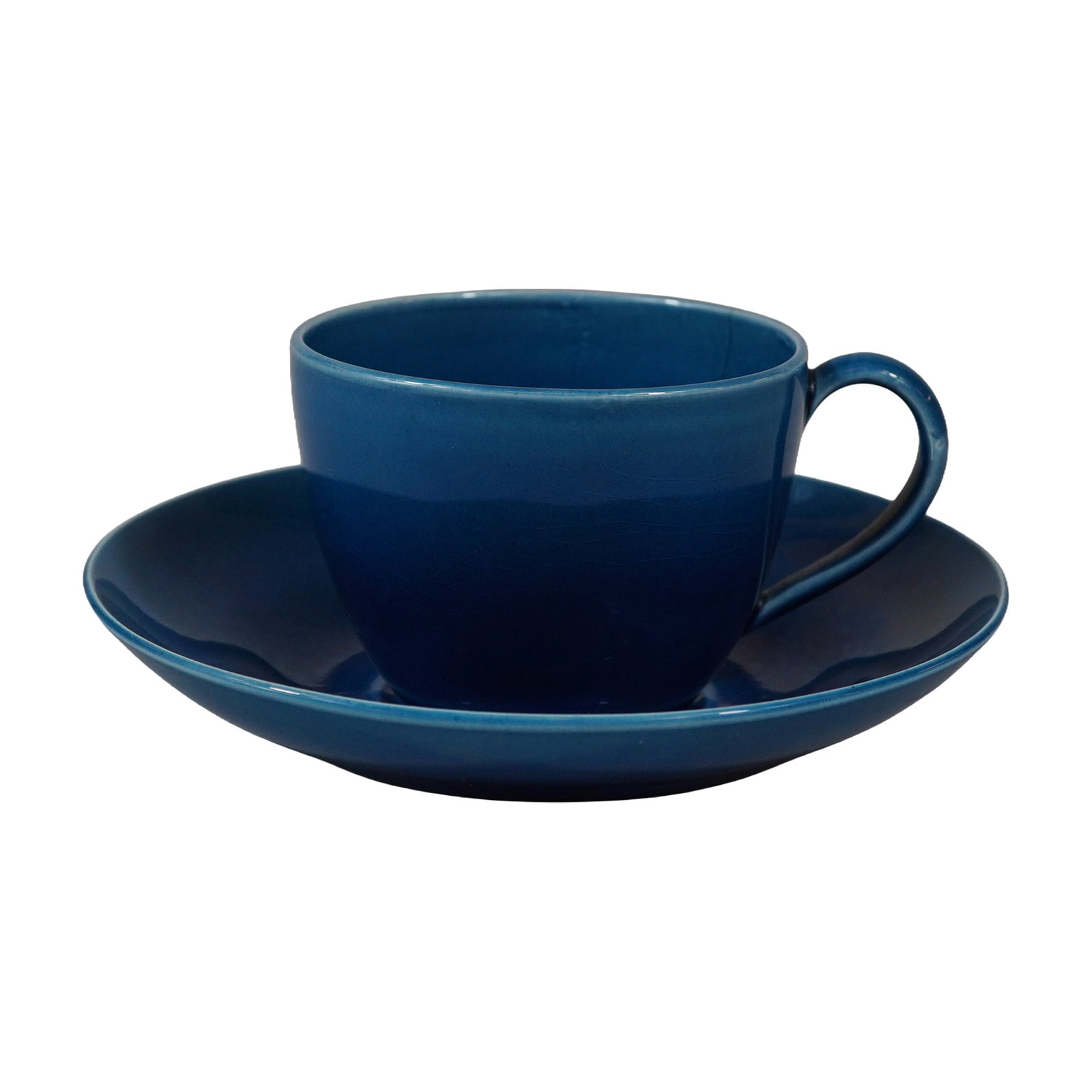 A Wedgwood Blue Glazed Majolica Cup and Saucer: This earthenware teacup and saucer set was produced by Wedgwood and is finished in a monochrome cobalt blue lead glaze, a style the manufacturer included in their Majolica line. The teacup is formed w