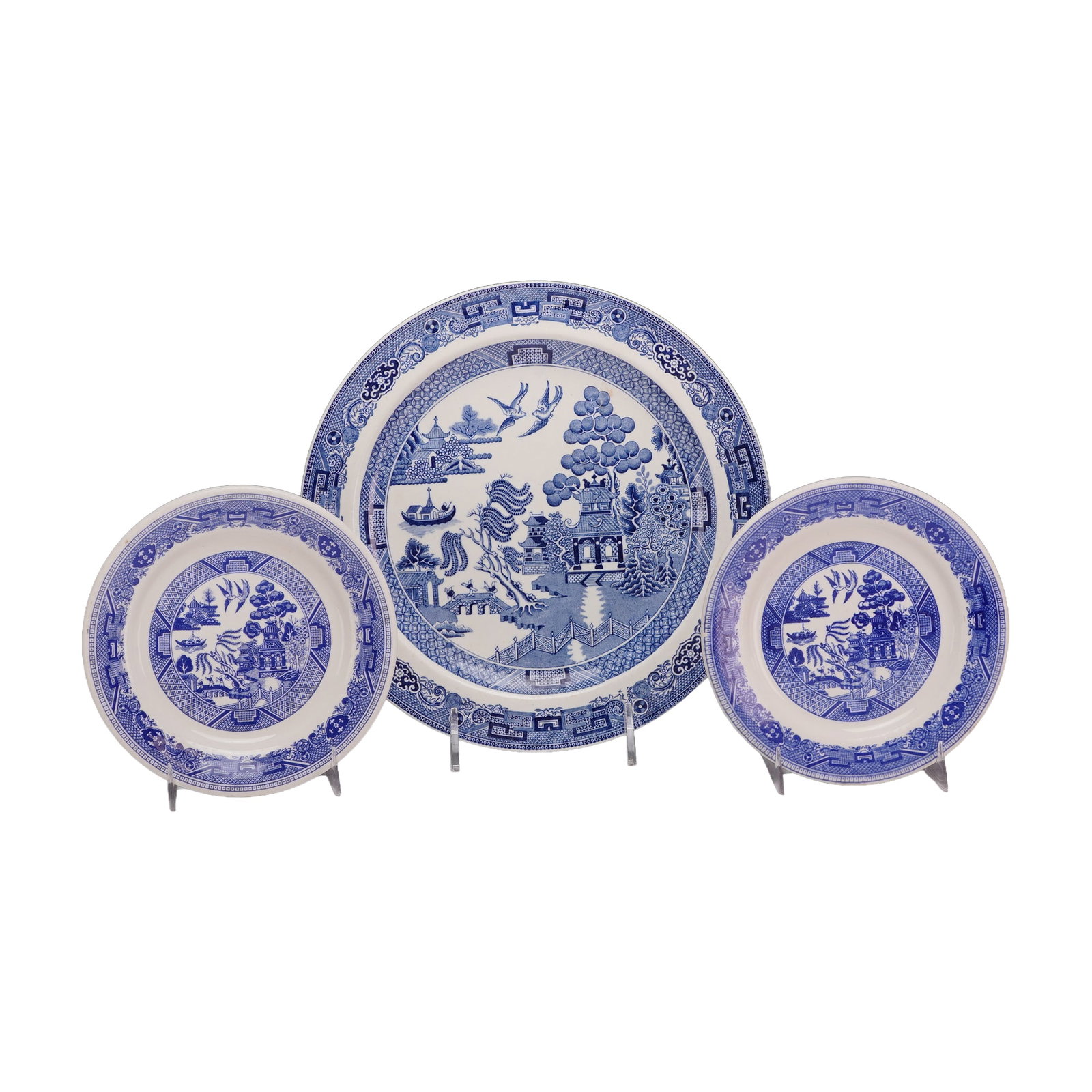 A Trio of Blue Willow Pattern Ceramic Plates by Wedgwood and Buffalo China: This trio of ceramic plates features the traditional Blue Willow pattern rendered in an underglaze blue transfer-print on a cream-colored ground. The central scene depicts the classic narrative elemen