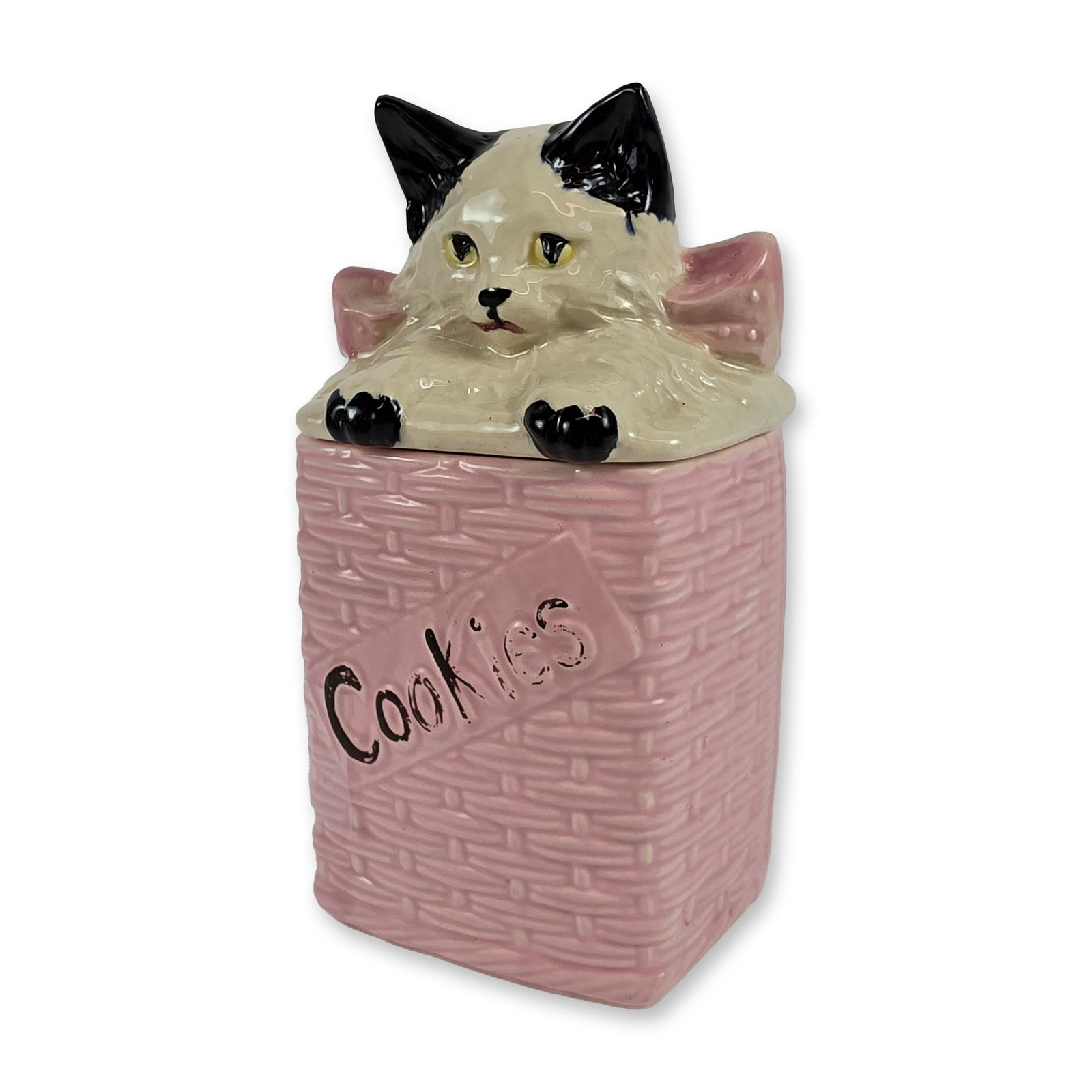 McCoy Ceramic Kitty Cat Basket Cookie Jar: The rectangular body features a pink glaze over a relief basketweave texture, with the word Cookies in black script on a front-facing plaque. The sculptural lid is formed as a white cat with black mar