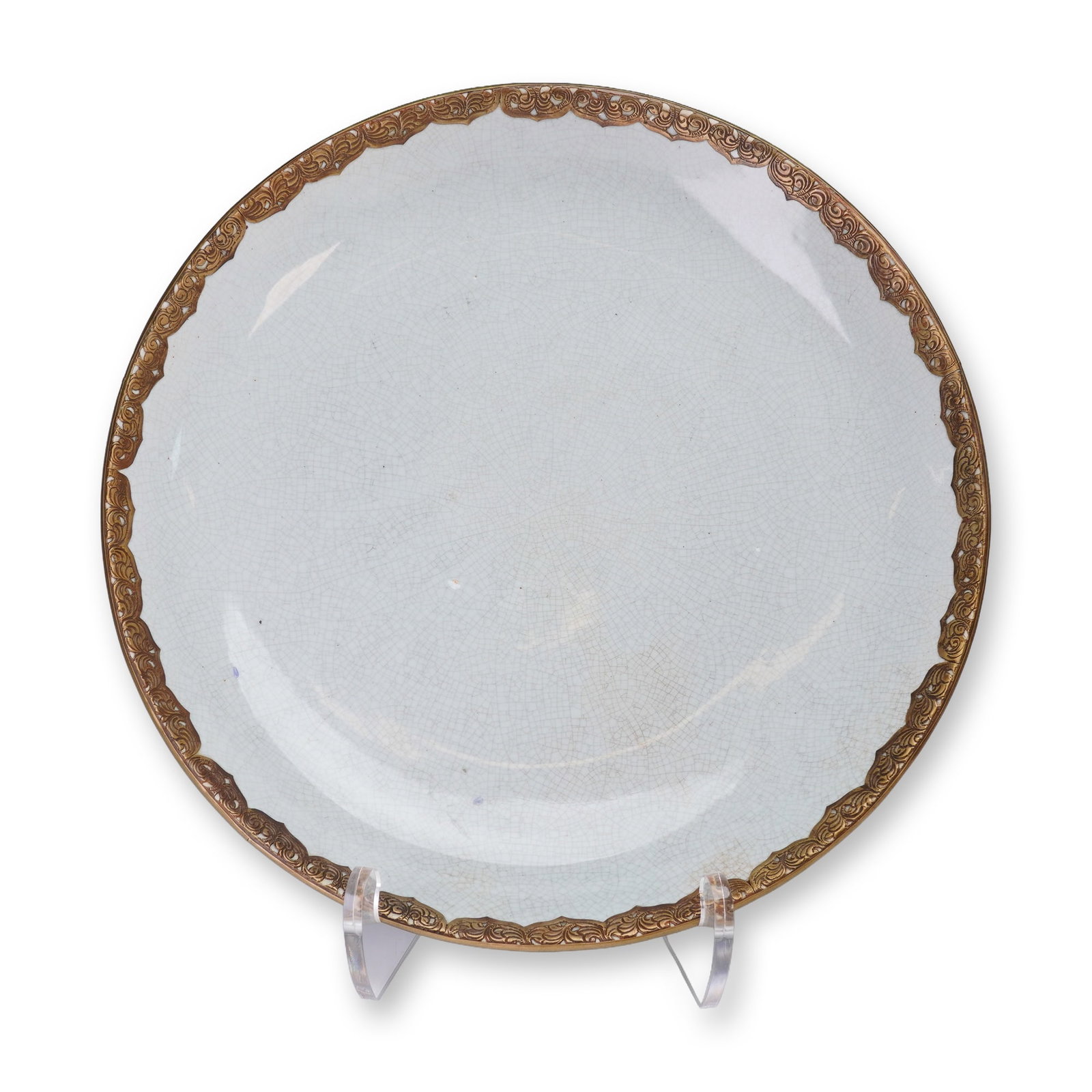 Metal-Mounted Crackle-Glazed Ceramic Charger: A circular charger covered in a pale light white glaze exhibiting extensive, fine crackling across the entire surface. The plate is distinguished by a heavy, applied metal mount, which forms the rim t