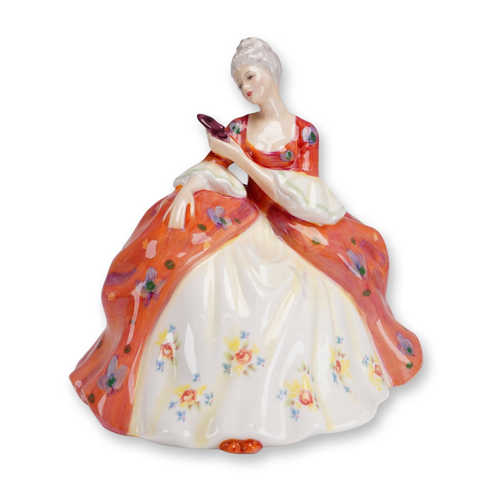 Royal Doulton Figurine, Wistful HN2396: The piece depicts a young woman in 18th-century period costume, seated in a contemplative pose with powdered white hair and holding a small purple masquerade mask. She wears a voluminous orange-red ov