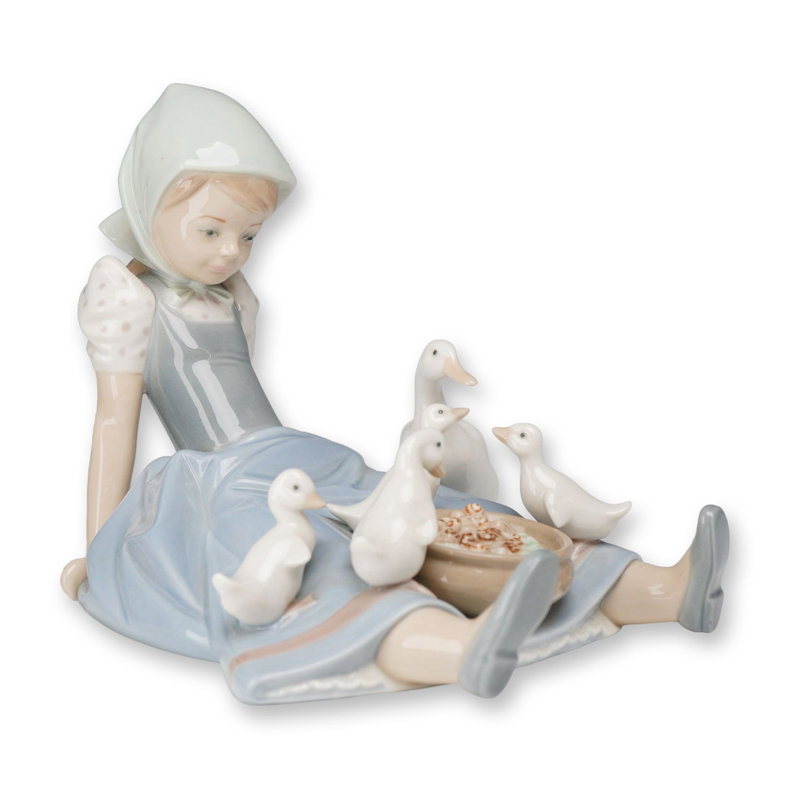 Lladro Porcelain Figurine, My Hungry Brood 01005074: This Lladro porcelain figurine, My Hungry Brood (01005074), features a glossy glazed finish and depicts a young village girl seated while feeding several ducklings gathered around her. The figure is m