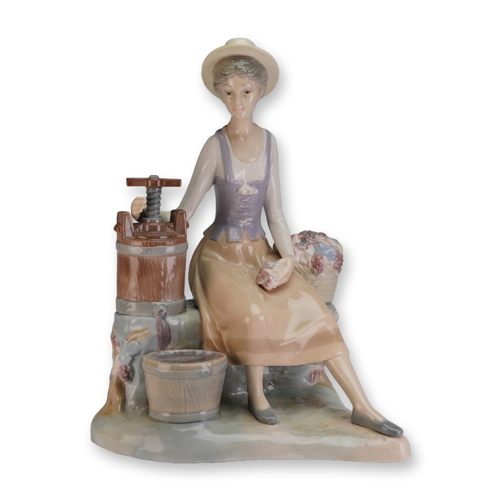 Zaphir Porcelain Sculpture, Woman with Wine Press: The piece depicts a young woman, or country lass, seated in pastoral attire next to a brown wooden fruit press. She is dressed in a wide-brimmed hat, purple bodice, and tan skirt. Beside the press is 
