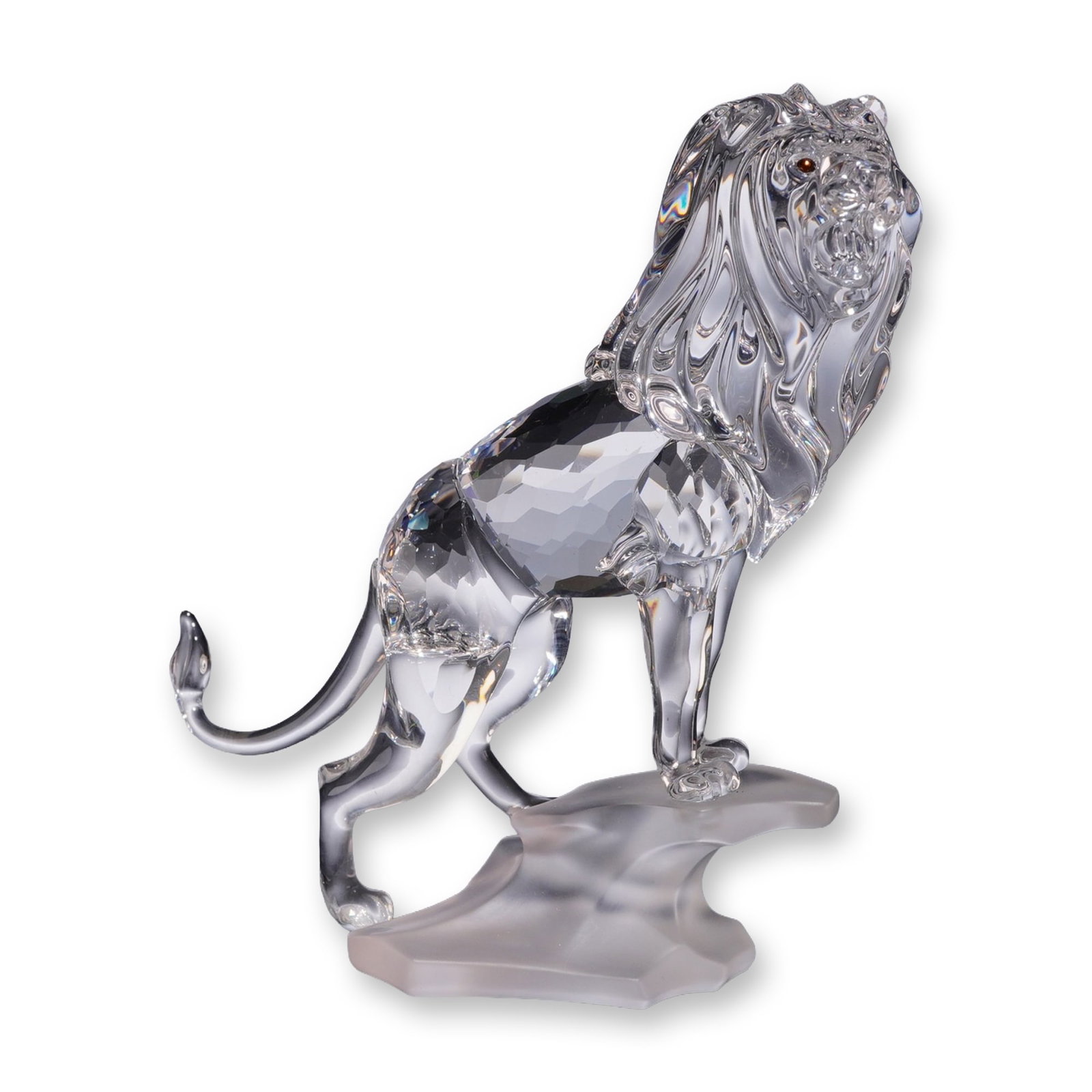 Swarovski Crystal Lion Figurine with Box: Swarovski crystal figurine depicting a standing lion. The figure features a faceted crystal body, a molded mane, and amber-colored crystal eyes, mounted on a frosted crystal base representing a rocky 