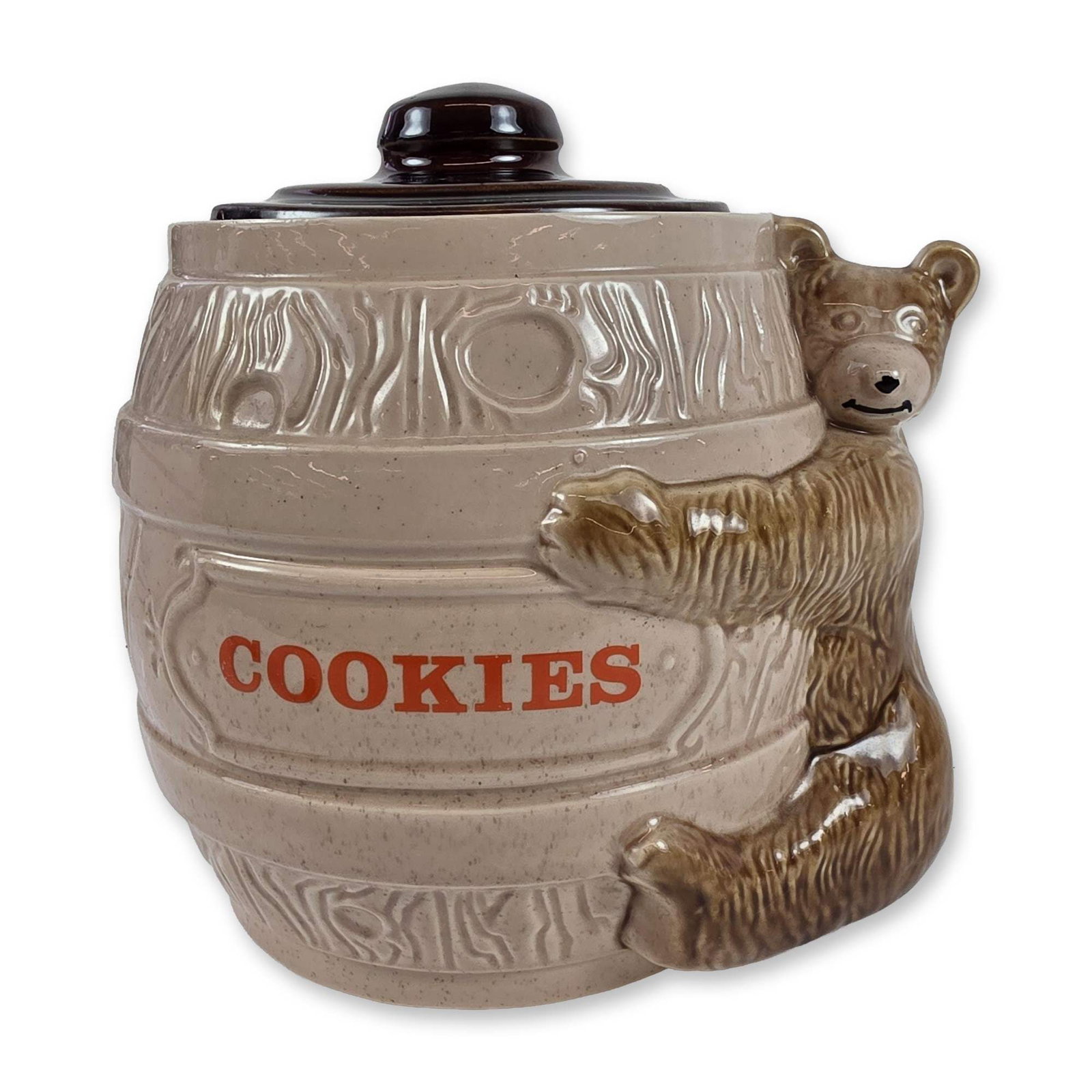 McCoy Ceramic Bear Cookie Jar: Ceramic cookie jar designed as a rustic wood-grain barrel with a relief-molded brown bear cub climbing the exterior. The vessel features a tan glaze with vertical red text reading COOKIES within a rai