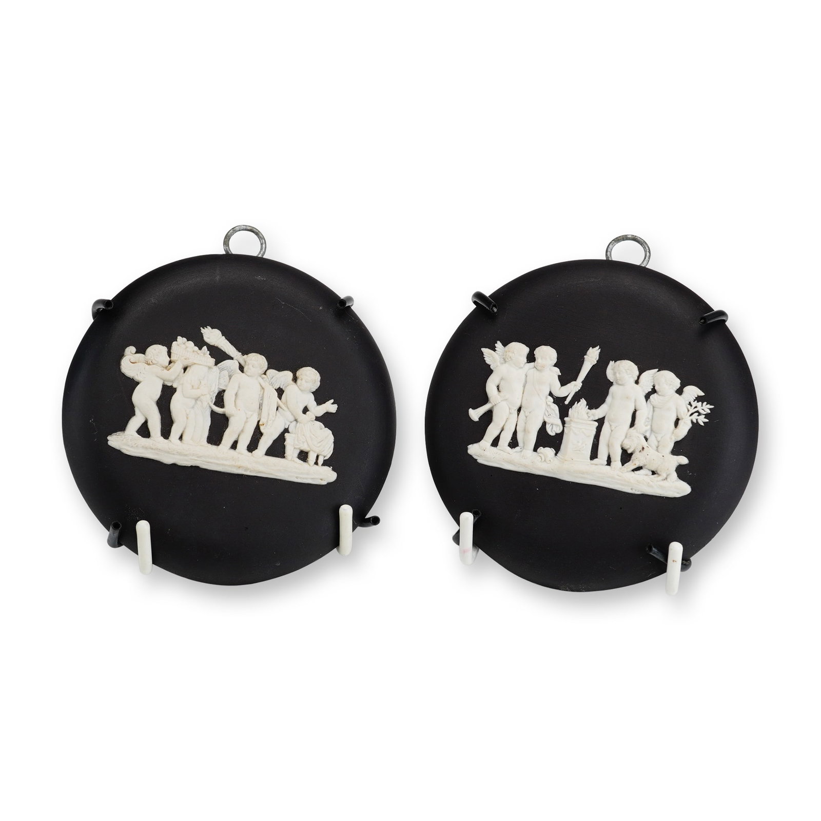A Pair of Wedgwood Black Basalt and White Jasperware Cupid Medallions with Hanging Components: This pair of circular medallions is manufactured by Wedgwood in England. The items are crafted from black basalt stoneware with applied white jasperware bas-relief decoration. One medallion depicts a 