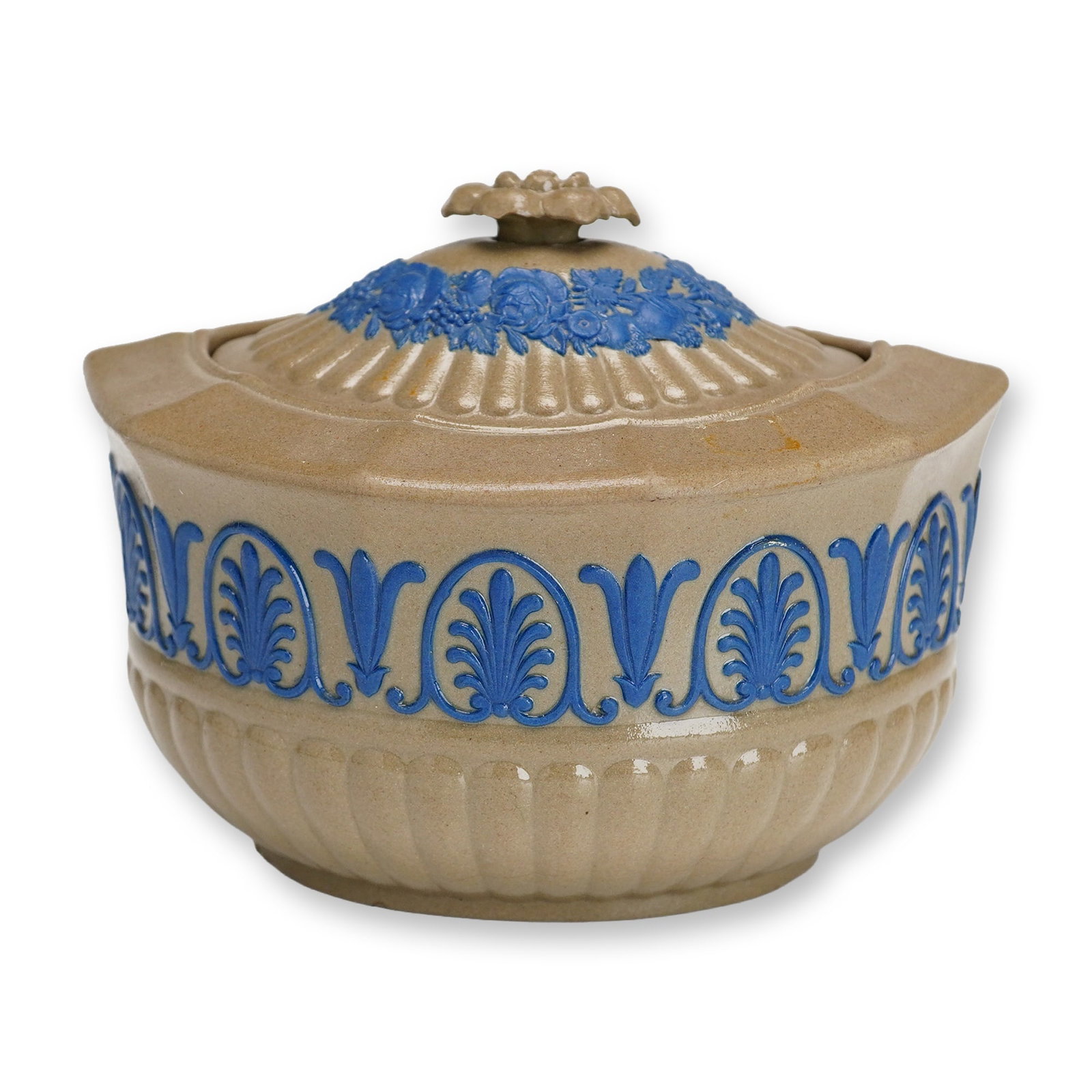 Wedgwood Caneware Lidded Sugar Bowl with Blue Relief Decoration: This lidded sugar bowl is produced by the Wedgwood factory in Staffordshire, England. The vessel is crafted from a buff-colored stoneware known as caneware, featuring an oval, lobed form. The lower ha