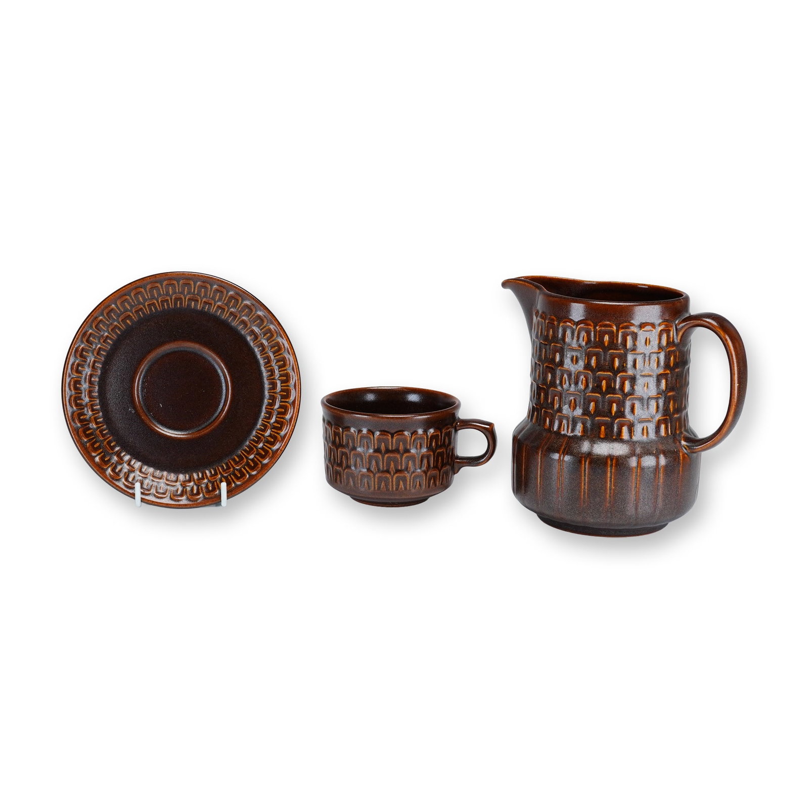 A Trio of Wedgwood Pennine Brown Stoneware Pieces including Pitcher, Cup, and Saucer: This three-piece set of stoneware was manufactured by Wedgwood in the Pennine pattern. The collection consists of one small pitcher, one flat cup, and one matching saucer. Each piece is decorated with