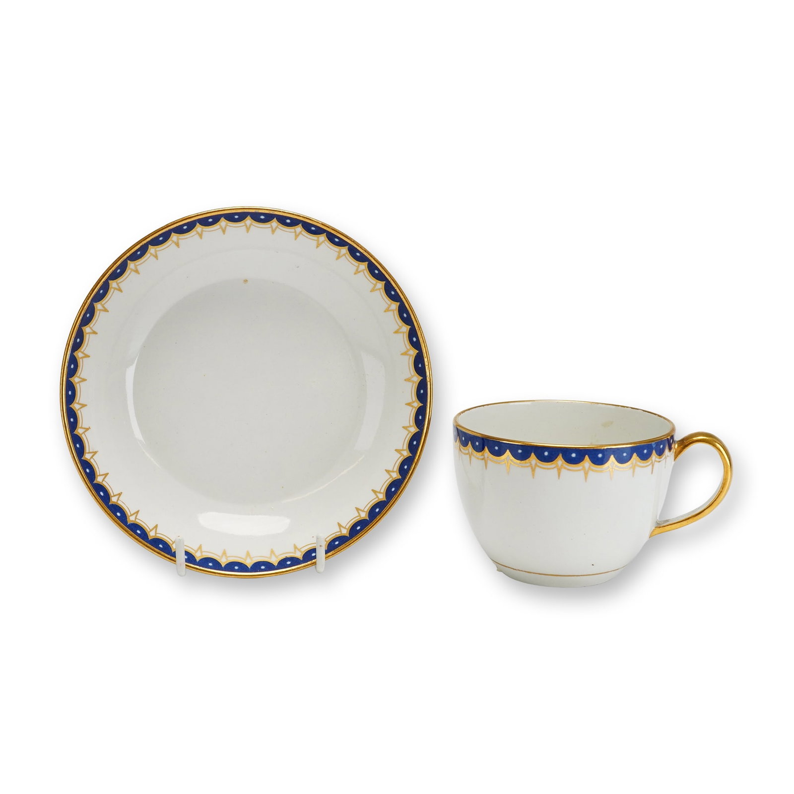 Wedgwood Porcelain Teacup and Saucer with Gilded Cobalt Scalloped Border: This set consists of a fine porcelain teacup and matching saucer manufactured by Wedgwood. The decoration features a refined neoclassical border with a cobalt blue band and a repeating scalloped edge.