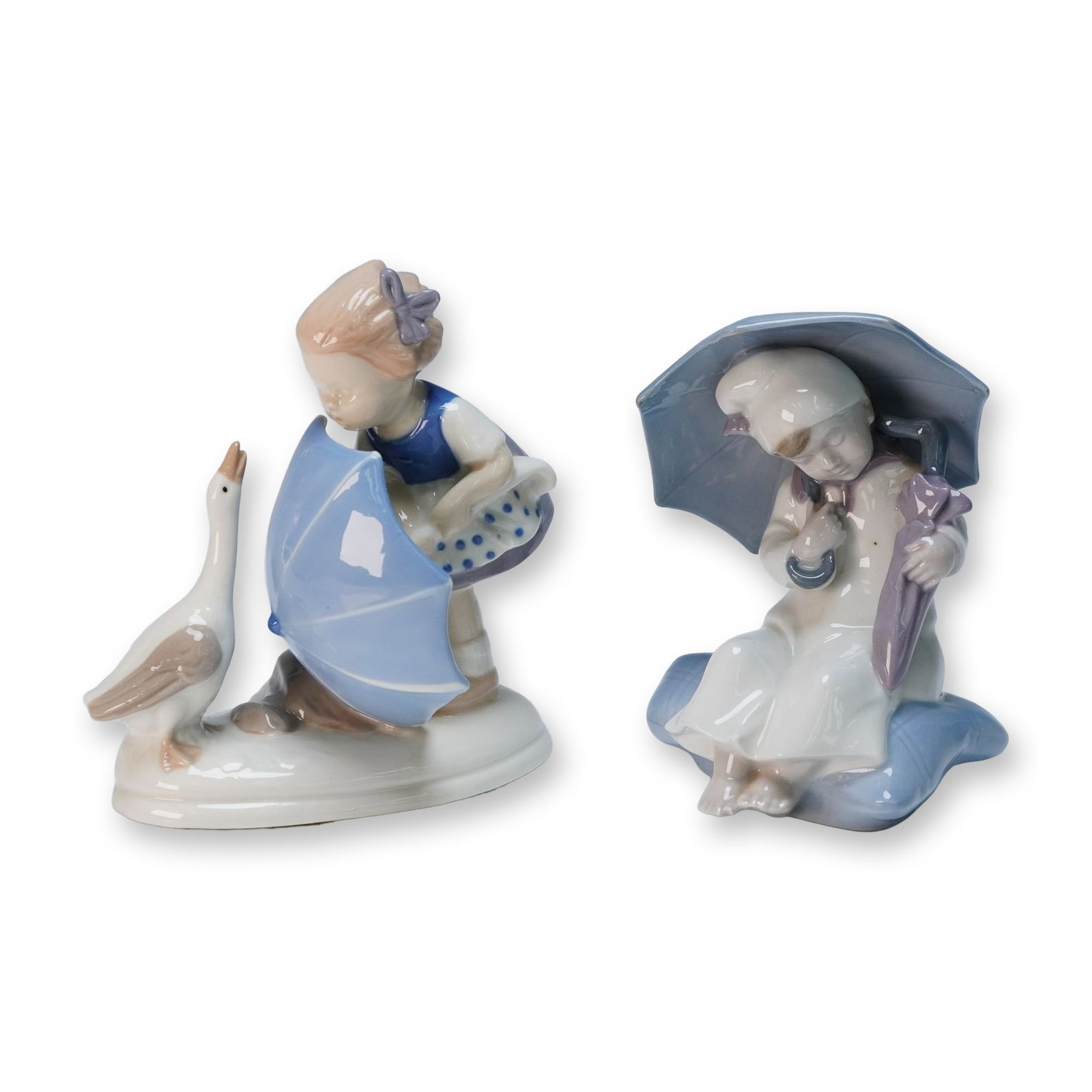 Carl Scheidig Porcelain Figurines - Girl w/ Goose & Seated Child: A pair of Carl Scheidig porcelain figurines, crafted from glazed porcelain in a pastel, stylized manner. The first figurine depicts a fair-haired girl in a blue and white dress, holding a light blue u