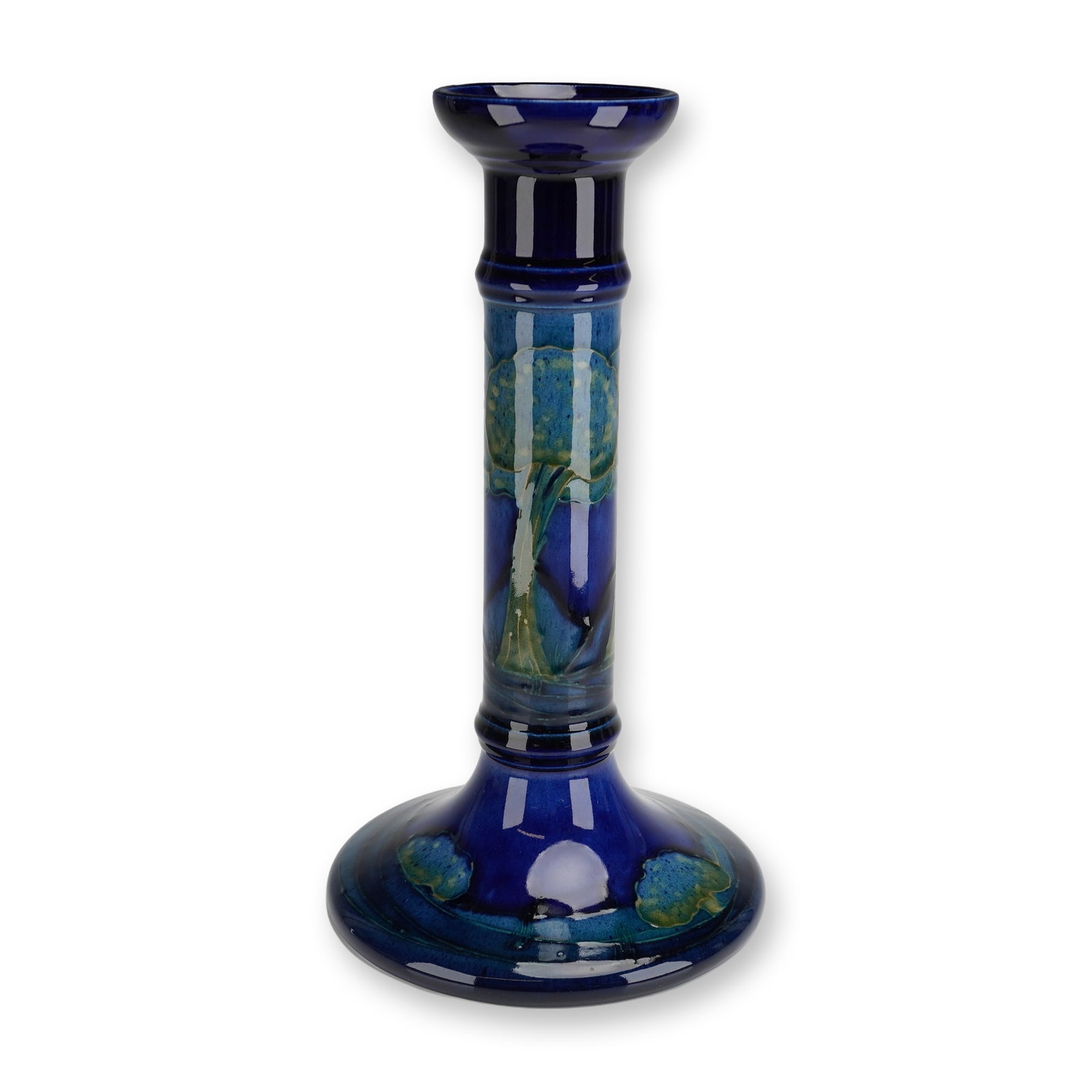 William Moorcroft Pottery Candlestick, Moonlit Blue: A William Moorcroft candlestick decorated in the Moonlit Blue pattern. The piece is tube-lined and finished in the deep, atmospheric blue glazes characteristic of the design, with stylized landscape m