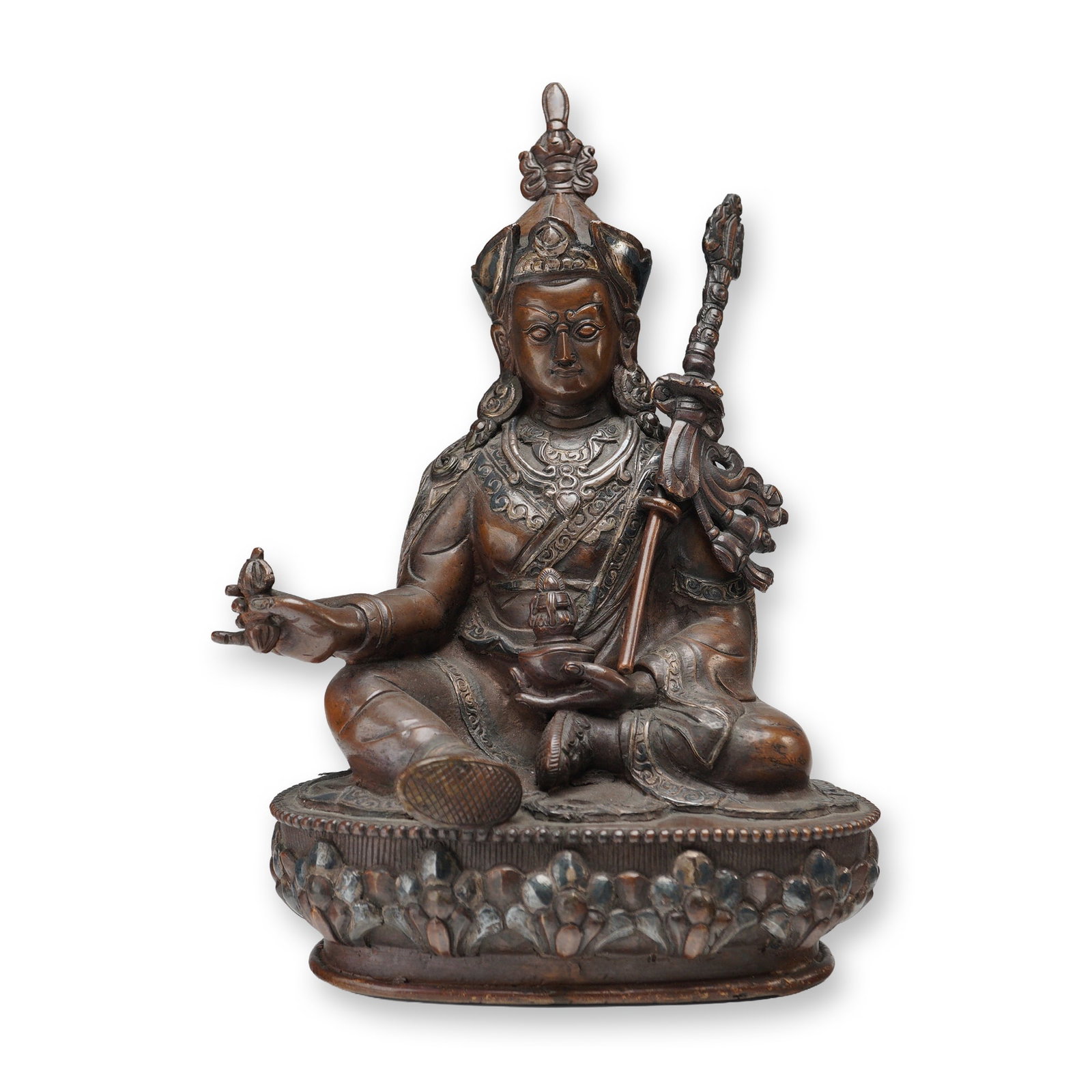 Tibetan Bronze Seated Deity with Silver Overlay: A Tibetan bronze figure of a seated deity, portrayed in a relaxed posture upon a lotus base, grasping a removable staff in one hand and a ritual object in the other. The figure is richly embellished
