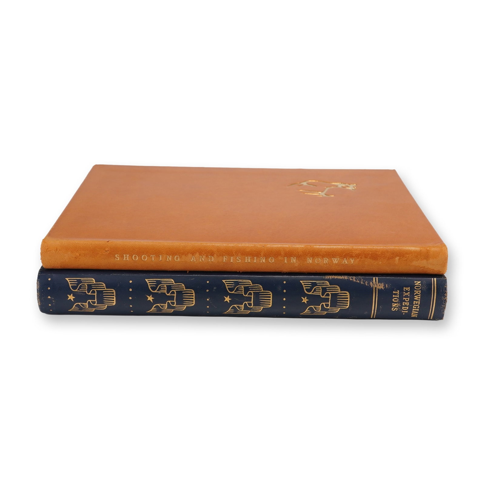2pc Norwegian Expeditions Hardcover Books: The first volume is bound in orange with the title Shooting & Fishing in Norway lettered in gold on the spine, featuring a small gold pictorial stamp of an animal on the front cover. The second