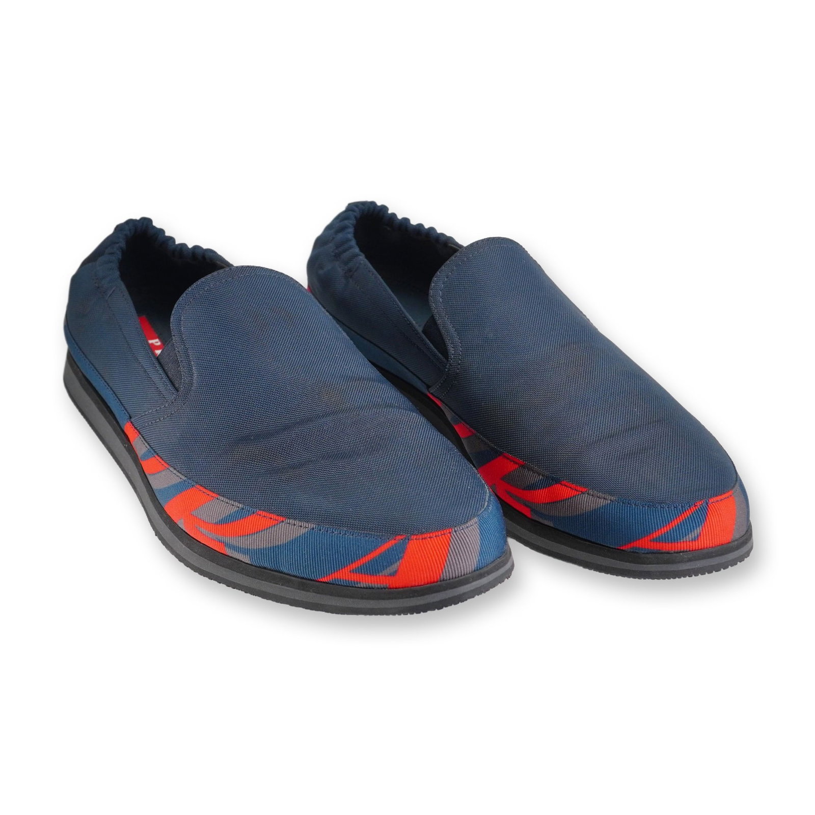 Prada Men's Navy Nylon Slip-On Sneakers: Prada men's slip-on sneakers, model 4D 2363, featuring navy blue nylon uppers and elasticated heels. Designed with a geometric patterned fabric trim in red, gray, and blue. The shoes are styled with a