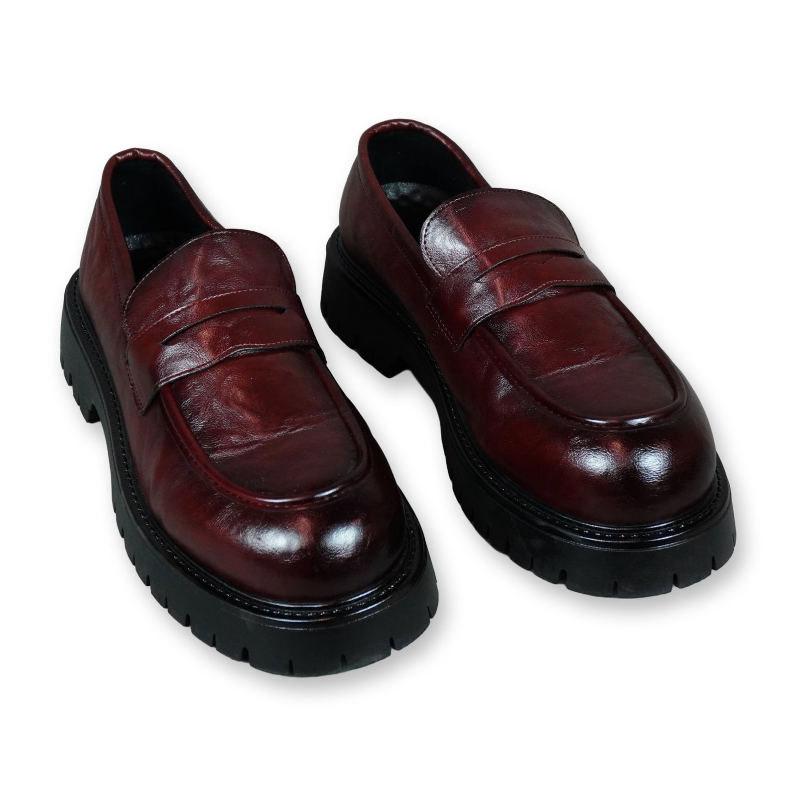 Pair of Burgundy Leather Lug Sole Penny Loafers: Pair of unbranded penny loafers in dark brown burnished leather with deep burgundy and oxblood tones. The shoes feature a prominent chunky black rubberized lug sole and classic penny strap detailing. 