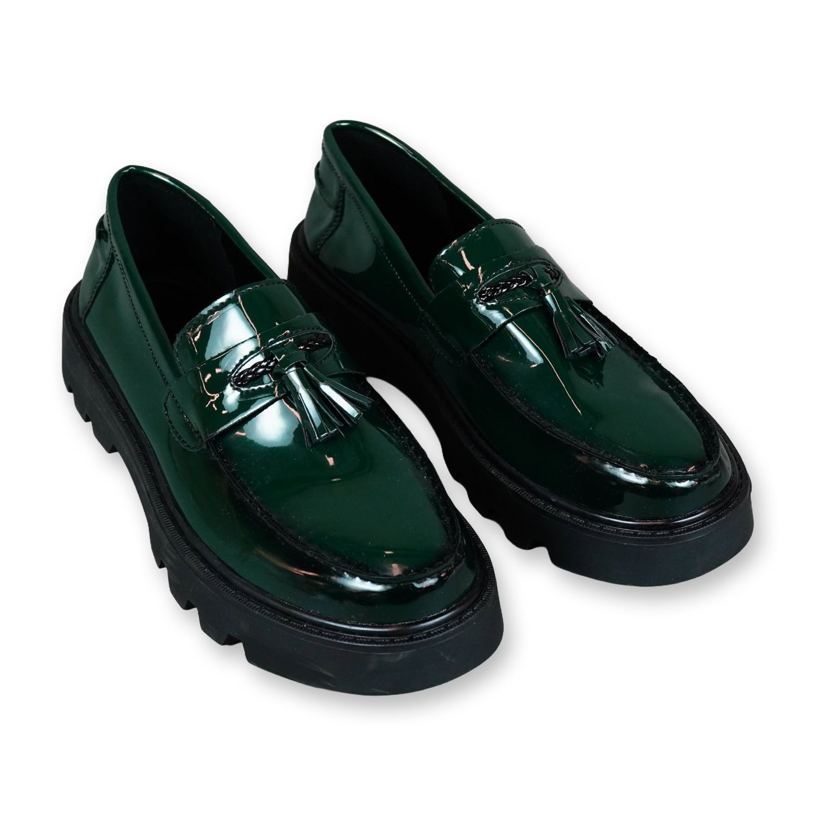 Pair of Green Patent Leather Tassel Loafers: A pair of contemporary unbranded tassel loafers in dark green patent leather, featuring a prominent chunky black rubber lug sole and platform. The slip-on design is detailed with classic black tassels