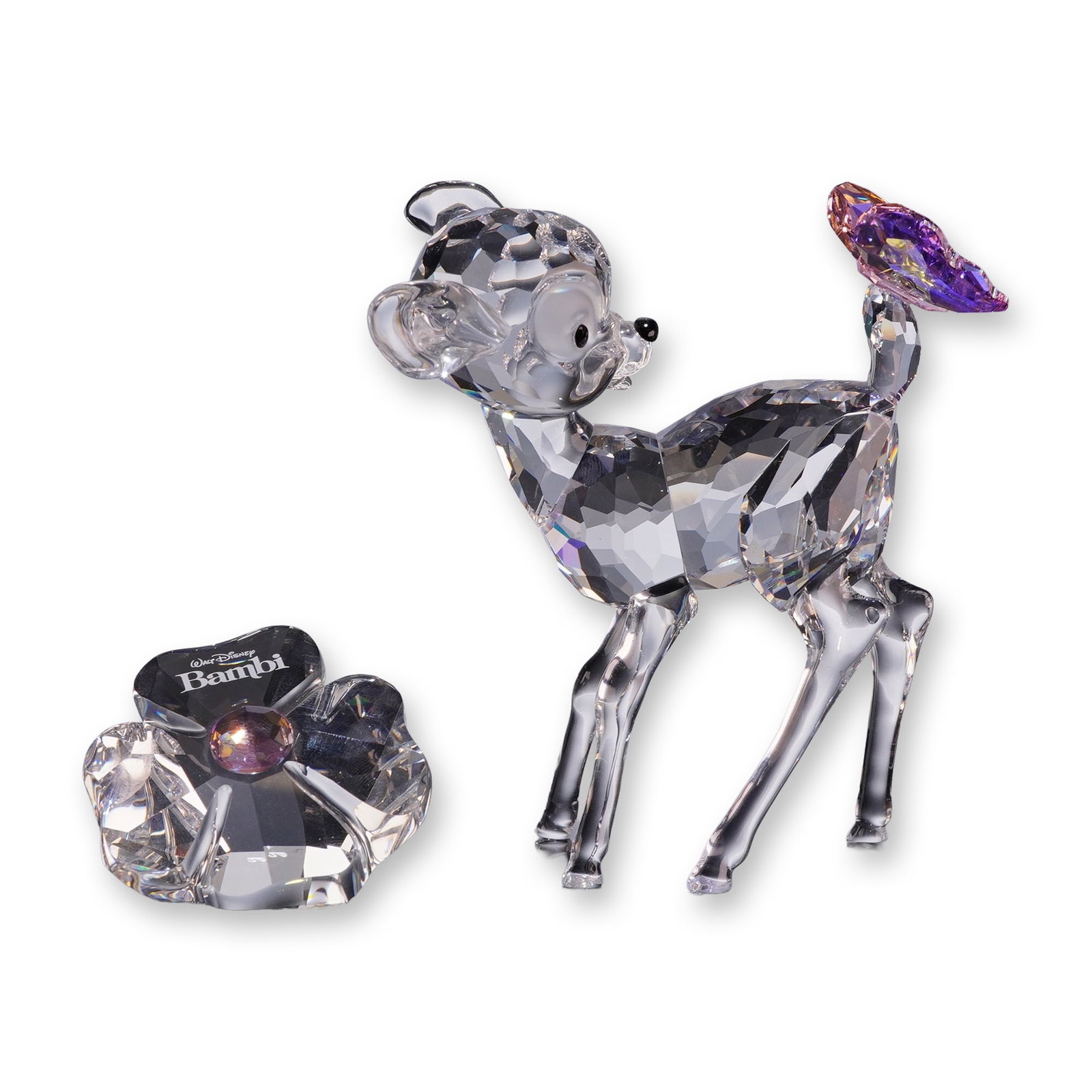 2pc Swarovski Crystal Disney Bambi Figurine and Plaque with Boxes: Swarovski Disney Series crystal Bambi figurine set, featuring a faceted clear crystal fawn figurine and a coordinating wildflower title plaque. The fawn is depicted looking over its shoulder with blac