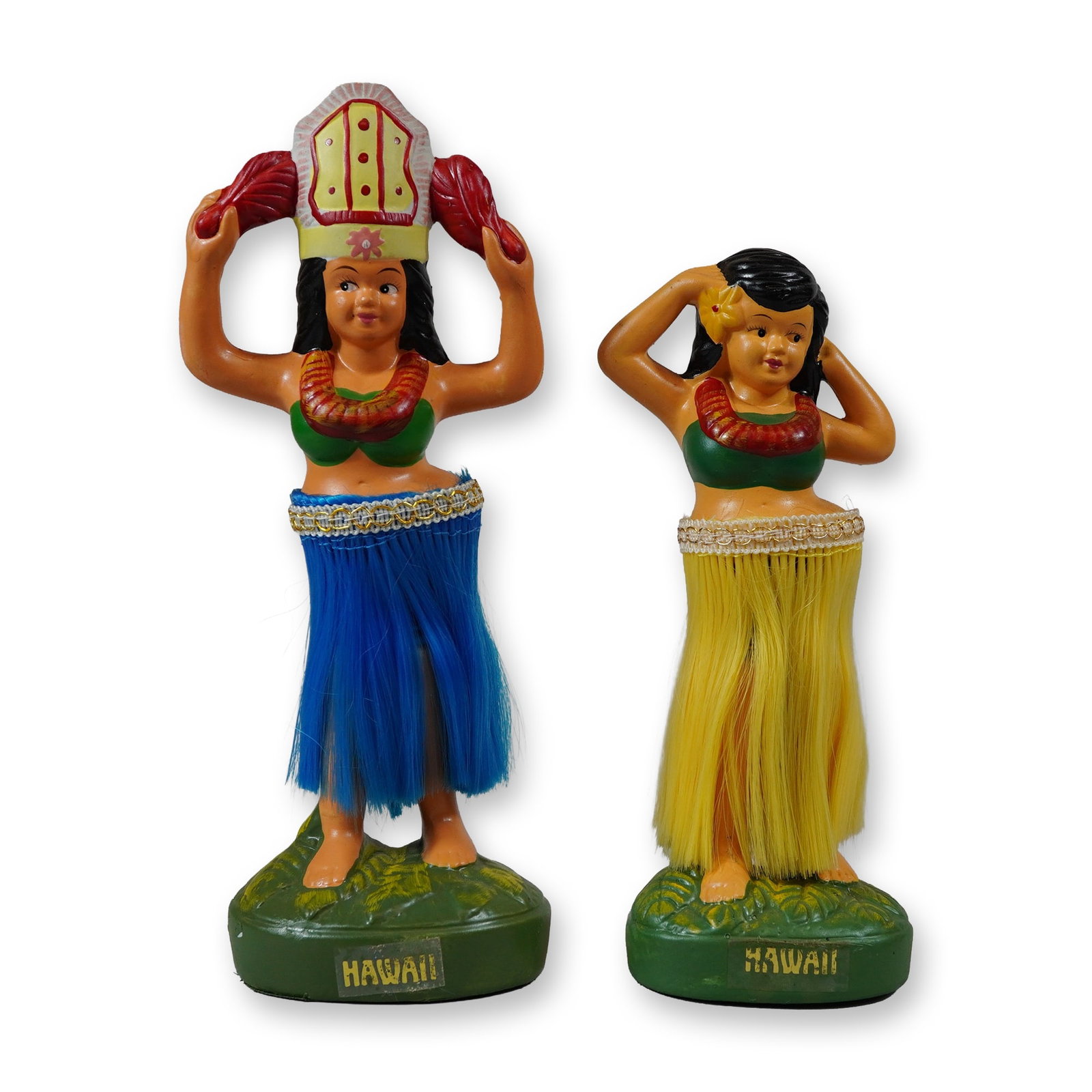 Pair of Vintage Hawaiian Chalkware Hula Girl Figurines: Mid-20th century souvenir style. Pair of hula dancer figurines in hand-painted molded ceramic or chalkware, each standing on a textured green base designed to resemble mossy ground. One figure is depi