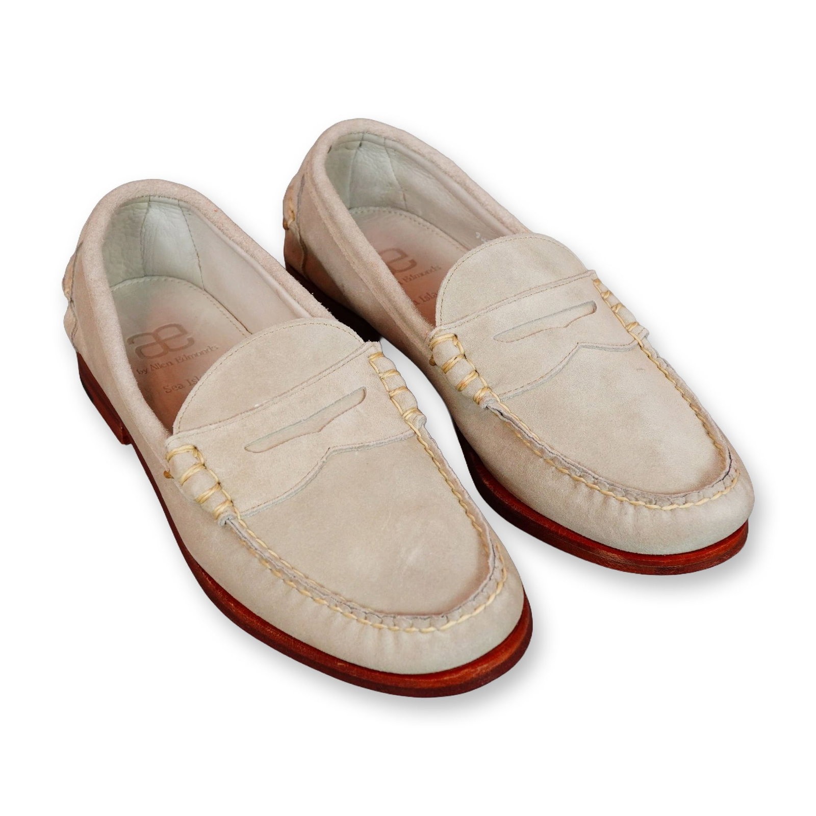 A Pair of Allen Edmonds Sea Island Suede Loafers: Allen Edmonds Sea Island penny loafers in light tan suede, featuring an unlined, soft-structured slip-on design with a traditional penny keeper strap across the vamp. Constructed with moc-toe stitchin