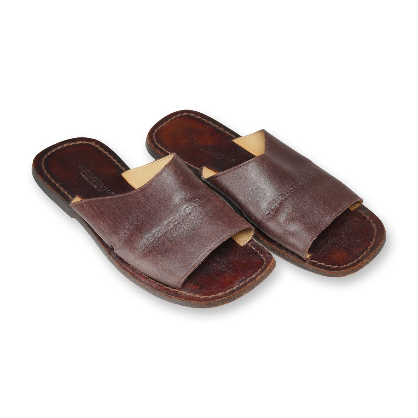 Pair of Dolce & Gabbana Leather Slide Sandals: Dolce & Gabbana. A pair of men's flat slide sandals in mahogany brown leather, featuring wide front straps with embossed branding. The dark brown leather footbeds feature contrast perimeter stitching 